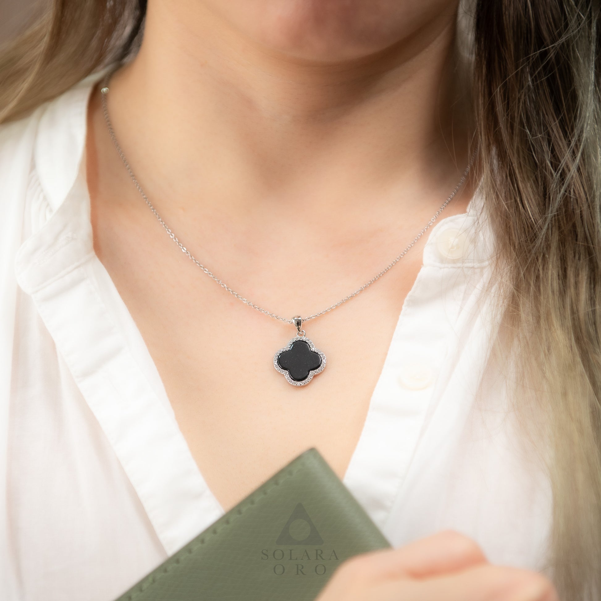 Person wearing a necklace with a clover-shaped pendant, holding a green book.