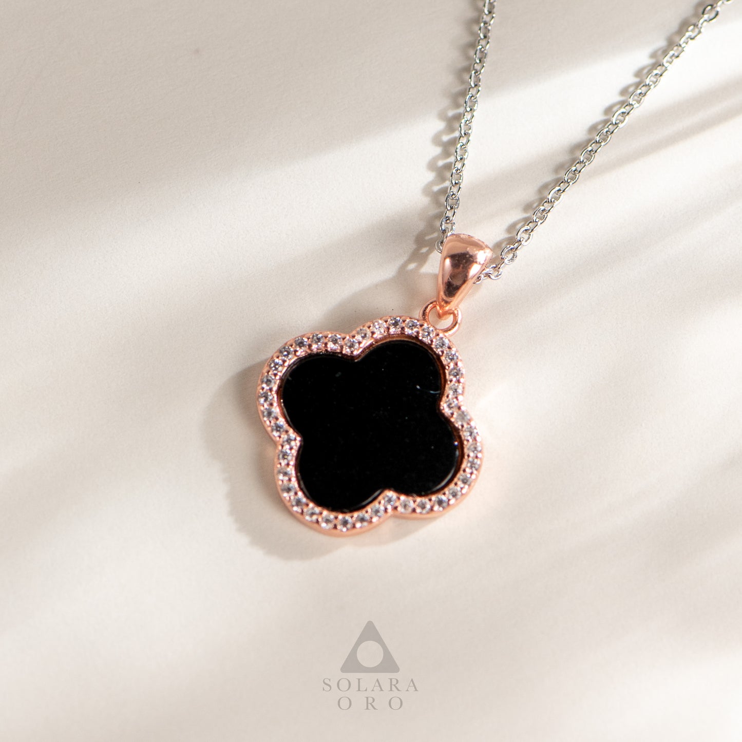 Necklace with a black clover pendant and rose gold border on a light background, featuring the Solara Oro brand.