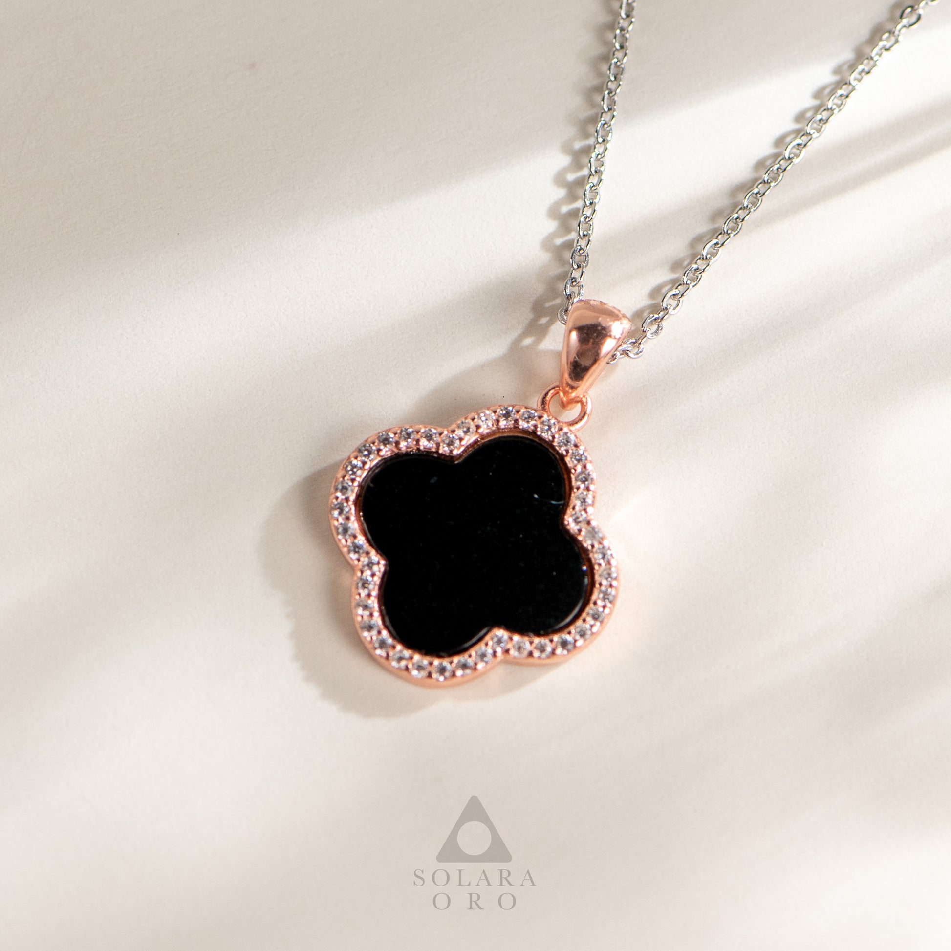 Necklace with a black clover pendant and rose gold border on a light background, featuring the Solara Oro brand.