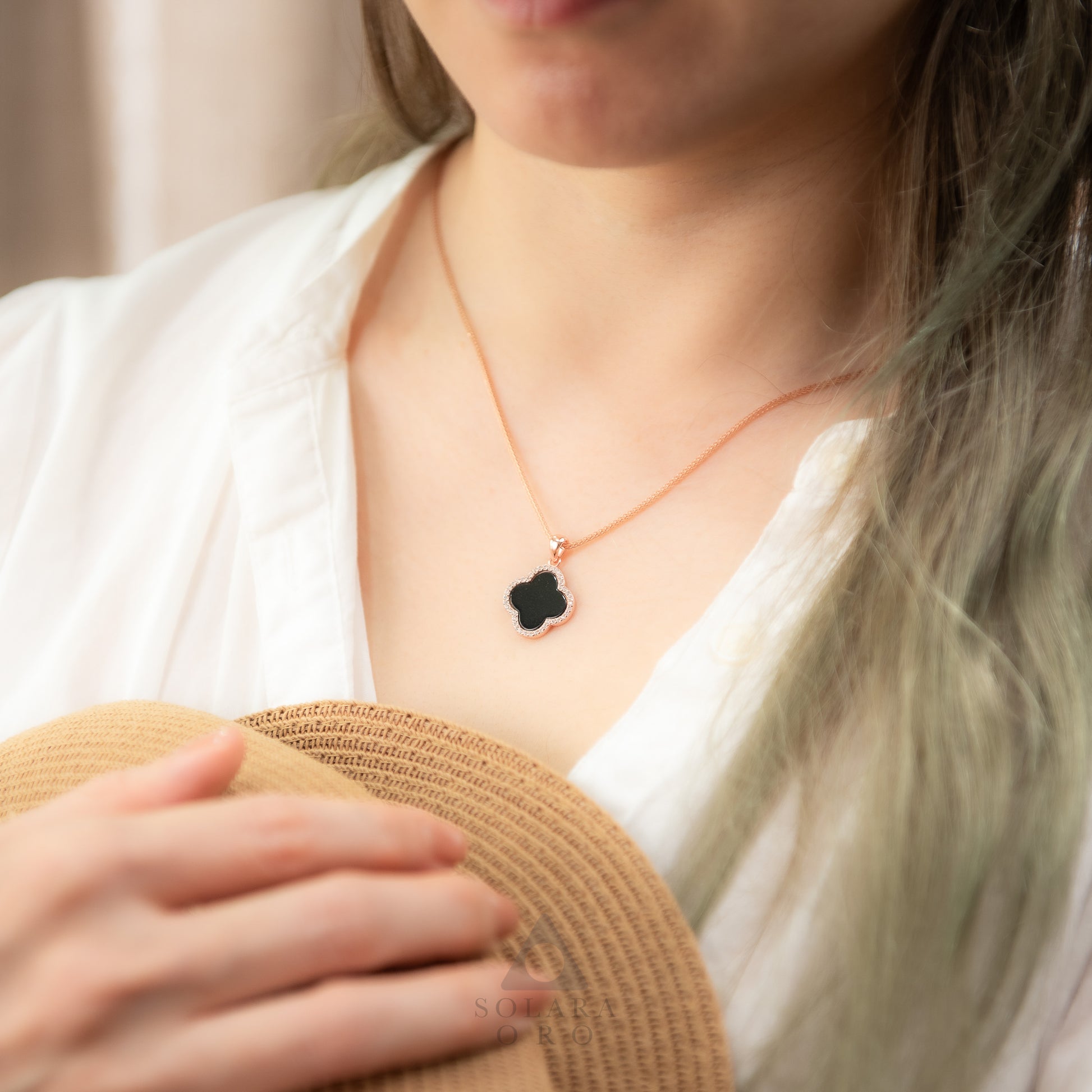 Person wearing a necklace with a black clover pendant