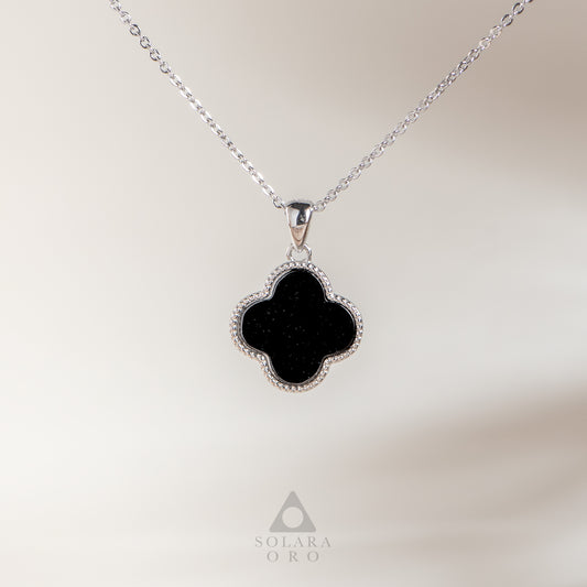 Black clover-shaped pendant on a silver chain with a blurred background