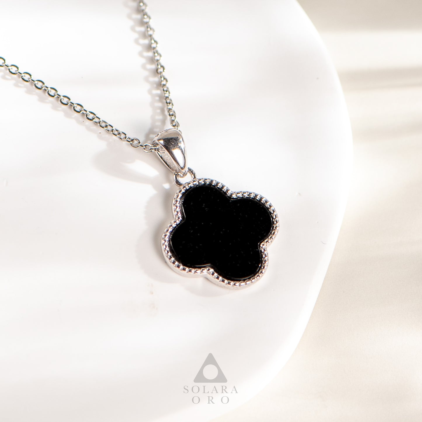 Black clover-shaped pendant on a silver chain with Solara Oro logo.