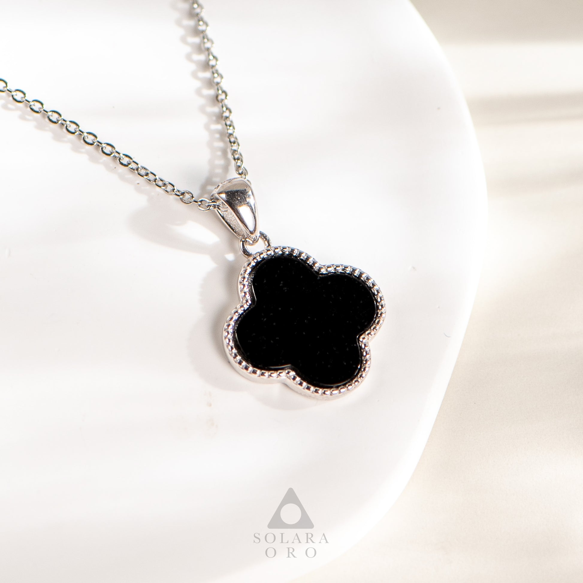 Black clover-shaped pendant on a silver chain with Solara Oro logo.