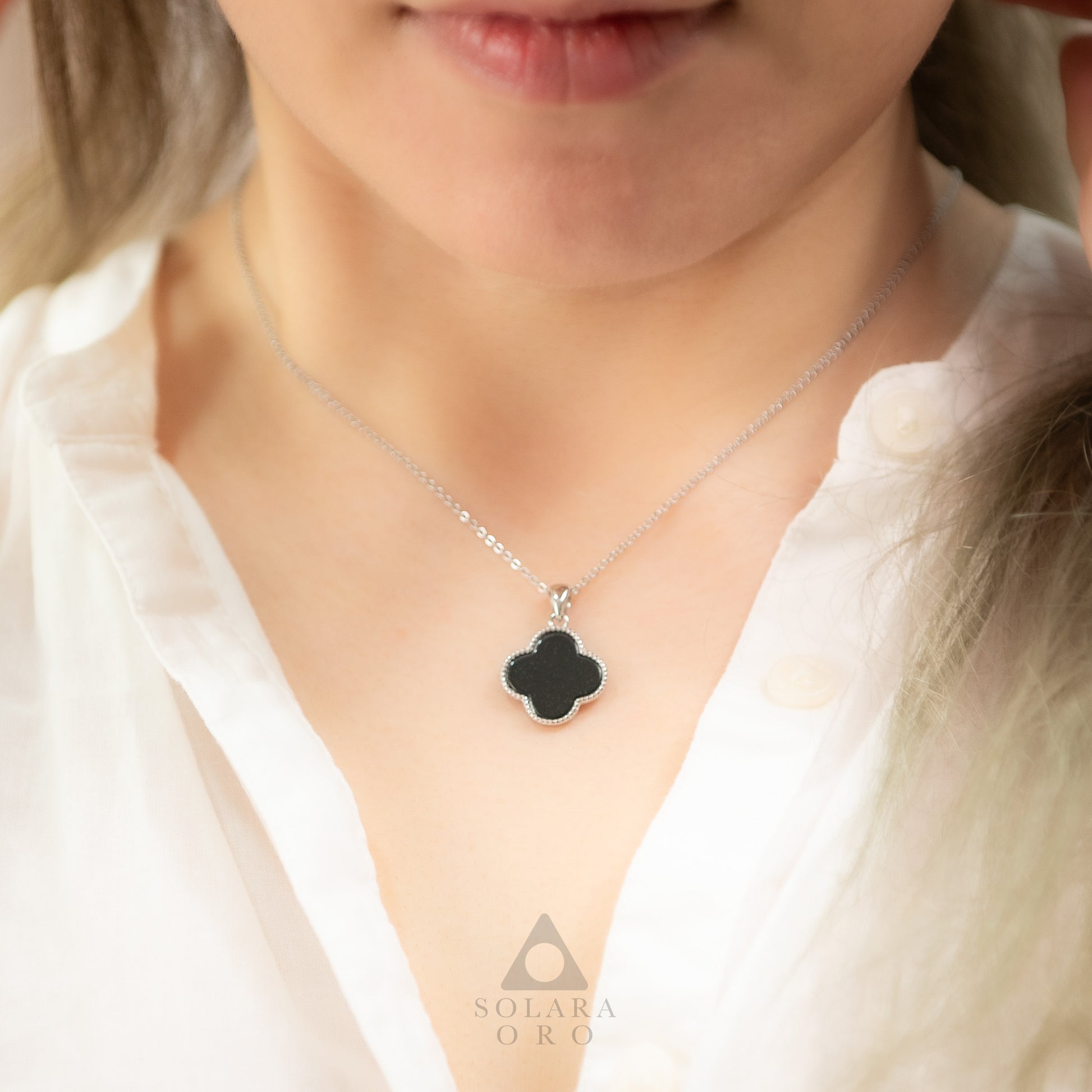Close-up of a necklace with a clover-shaped pendant worn by a person, with 'Solara Oro' branding.