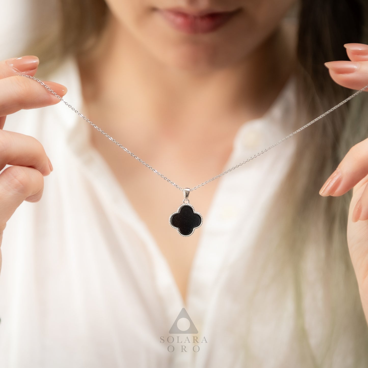 Black clover-shaped pendant on a silver chain held by a person wearing a white top.