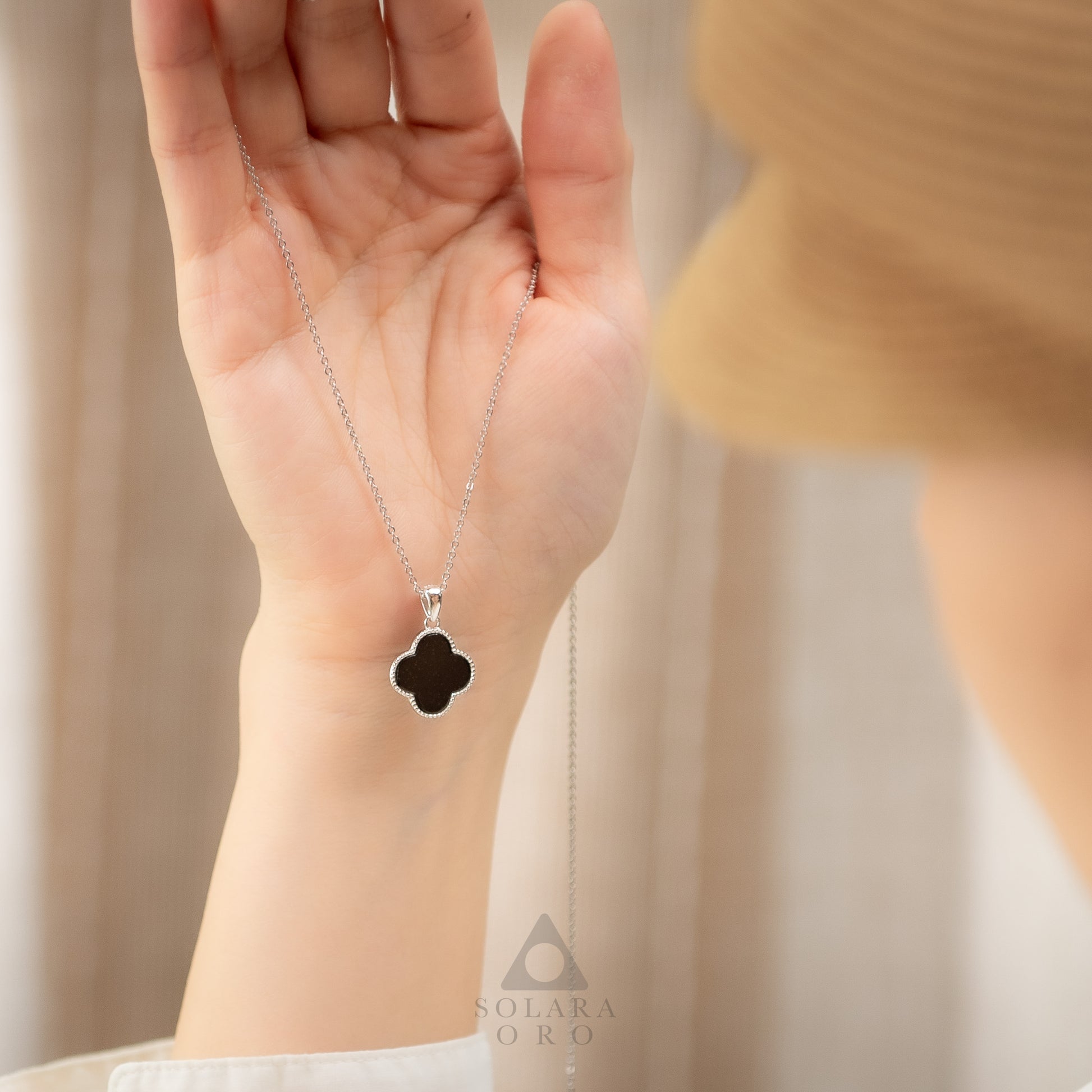 Hand holding a necklace with a clover-shaped pendant against a neutral background