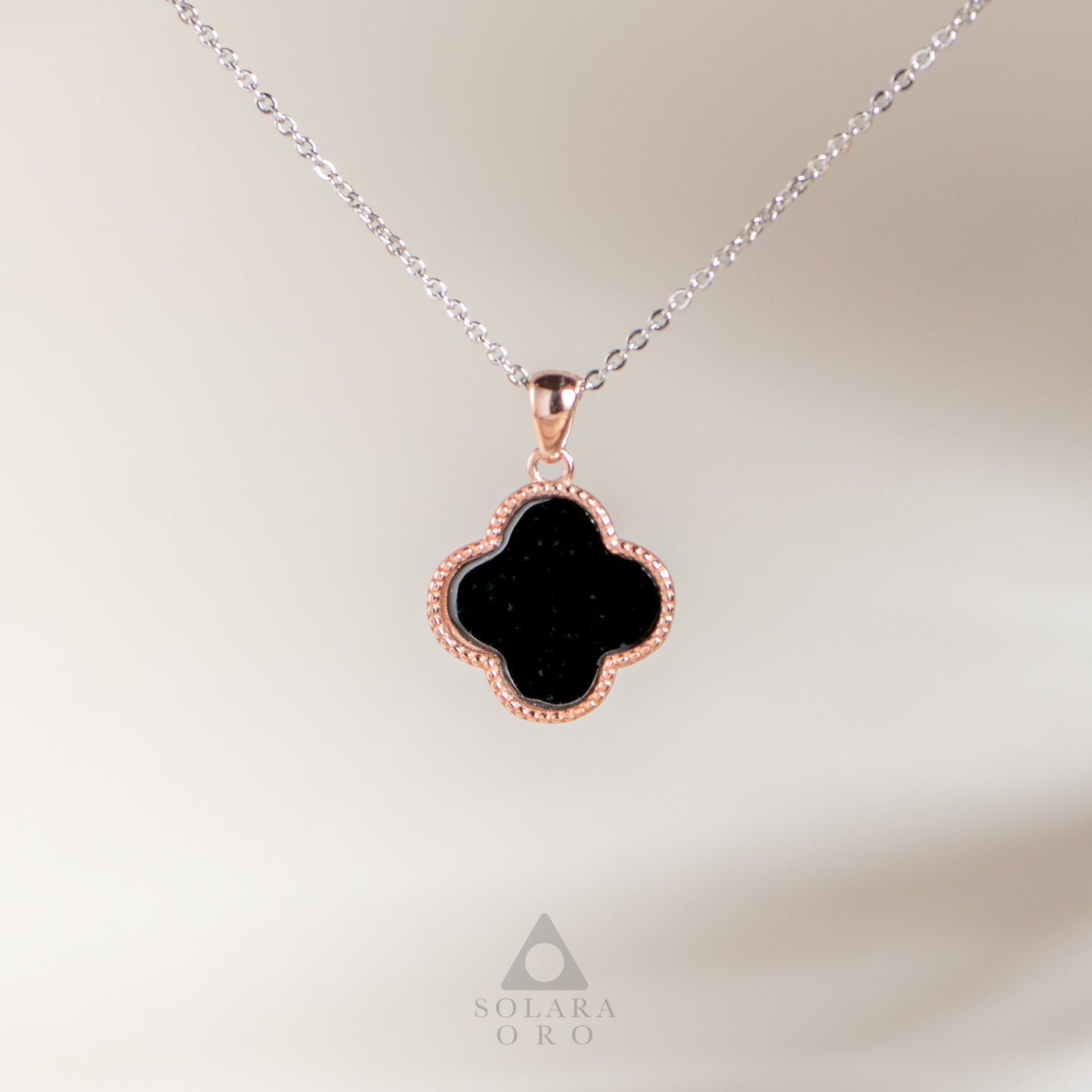 Black clover-shaped pendant on a silver chain with a blurred background