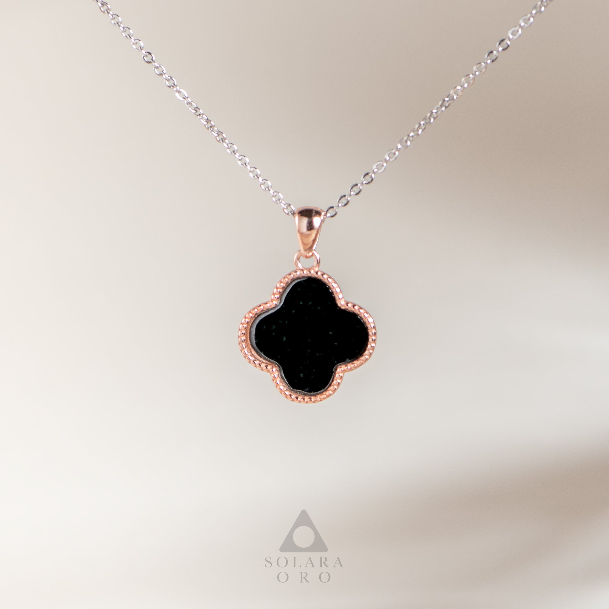 Black clover-shaped pendant on a silver chain with a blurred background