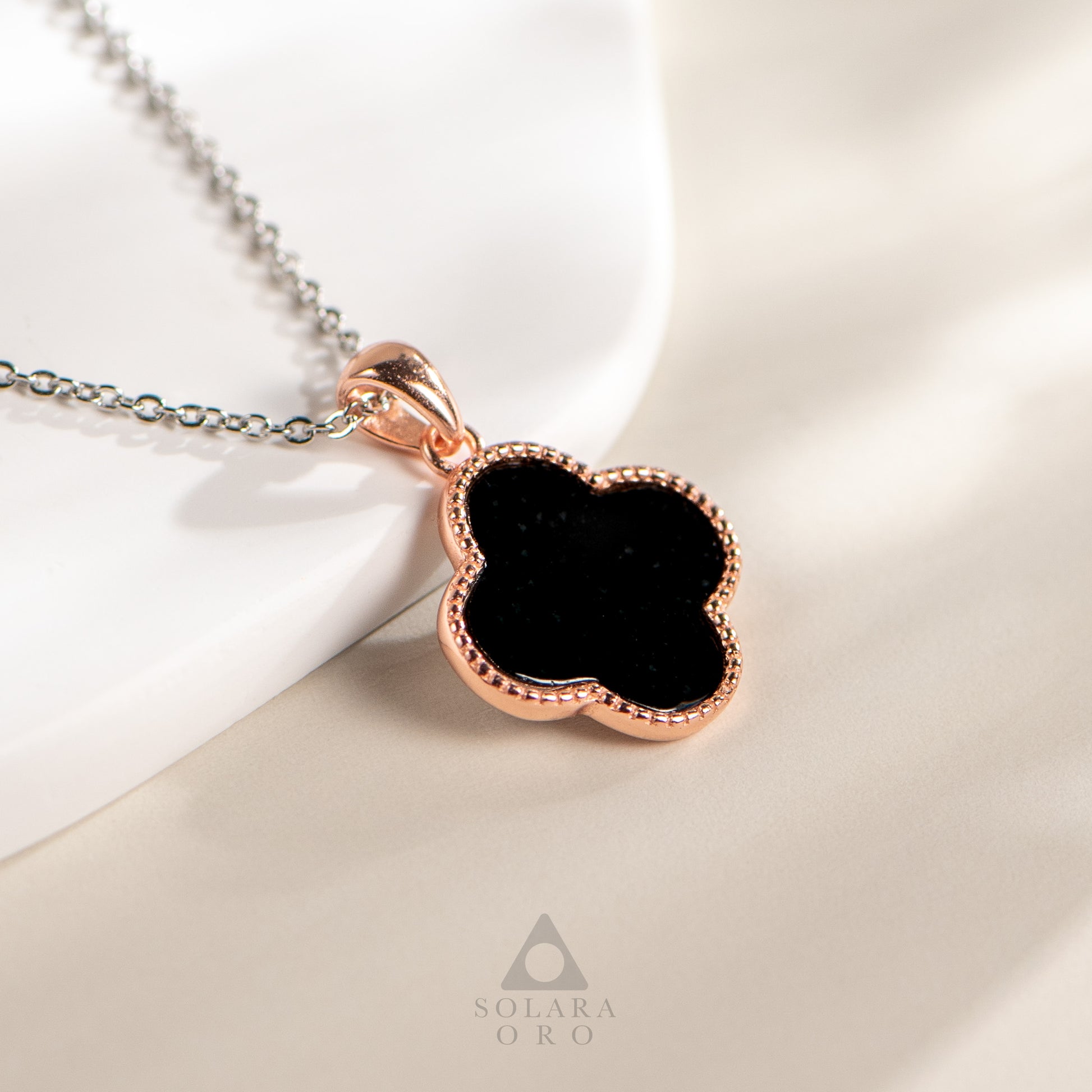 Rose gold necklace with black pendant on a soft white background