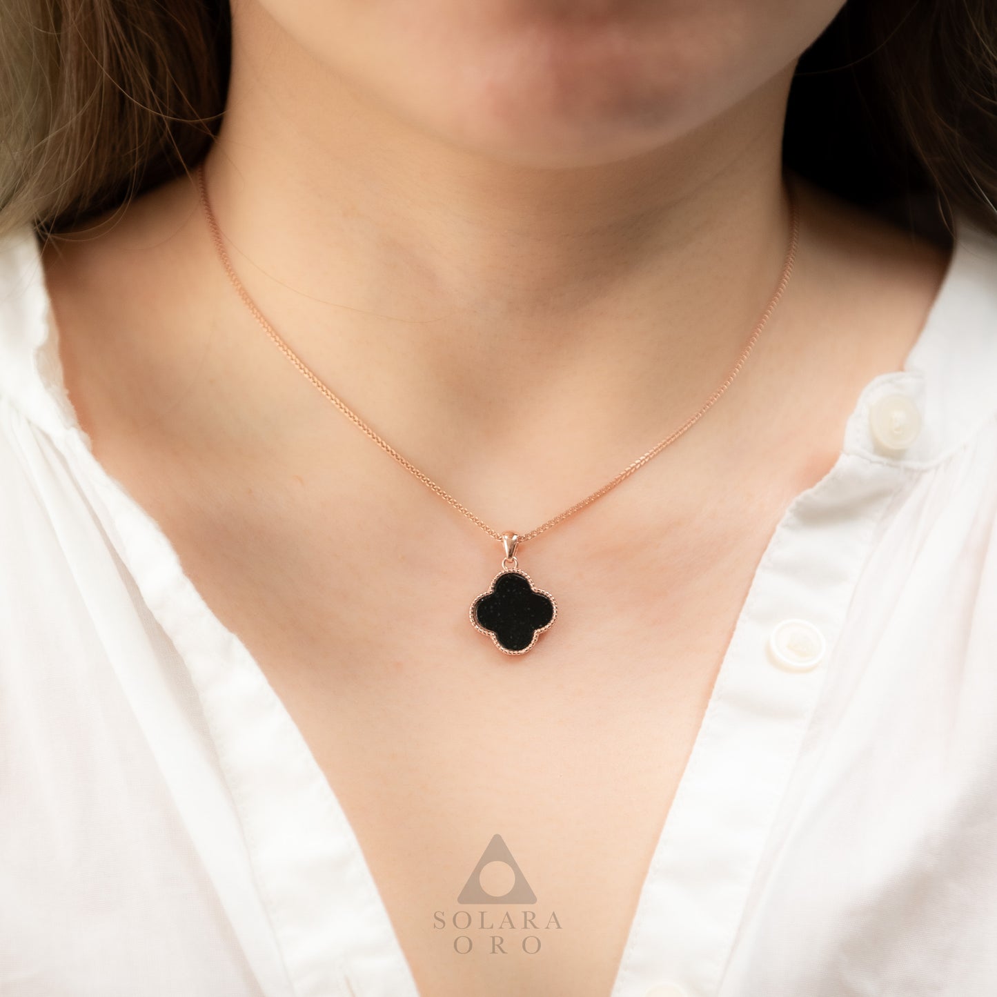 Rose gold necklace with a black clover pendant on a white shirt, featuring the Solara Oro brand.