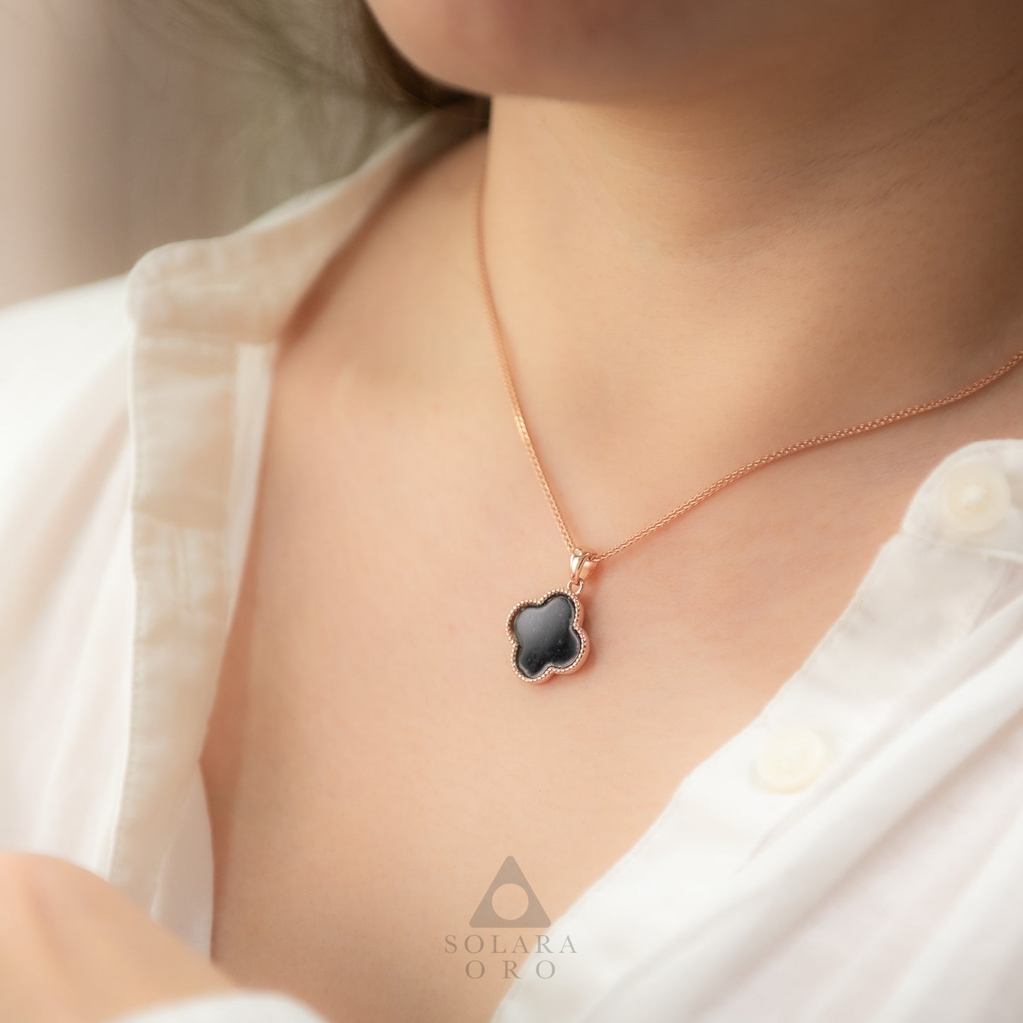 Necklace with a black clover pendant worn by a person, brand 'Solara Oro' visible.