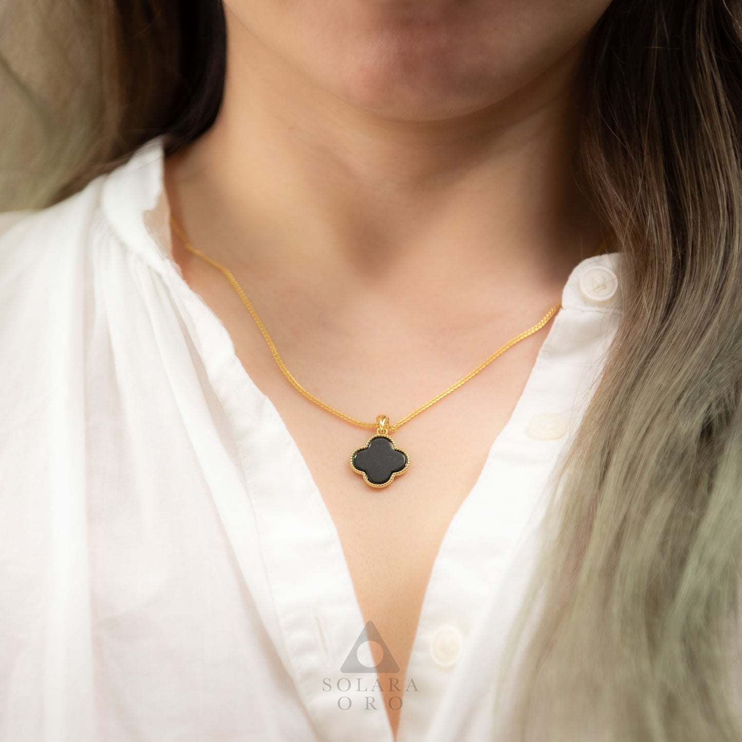Gold necklace with a black pendant worn by a person in a white shirt, with 'Soleara' branding.