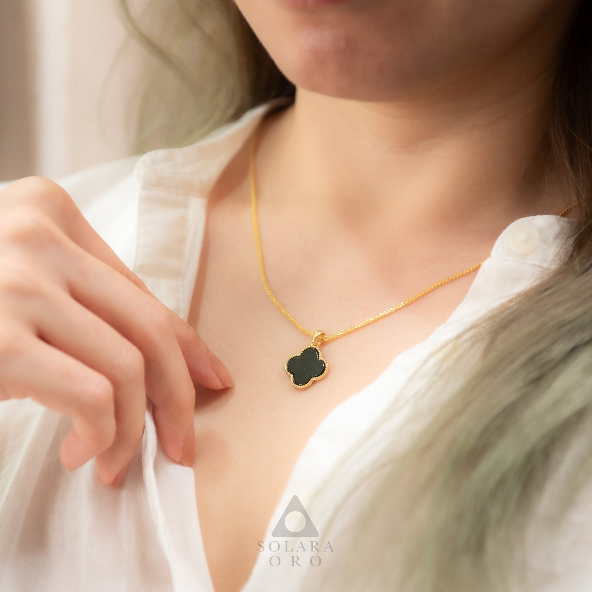 Person wearing a gold necklace with a black pendant, brand 'Soleara Oro' visible.