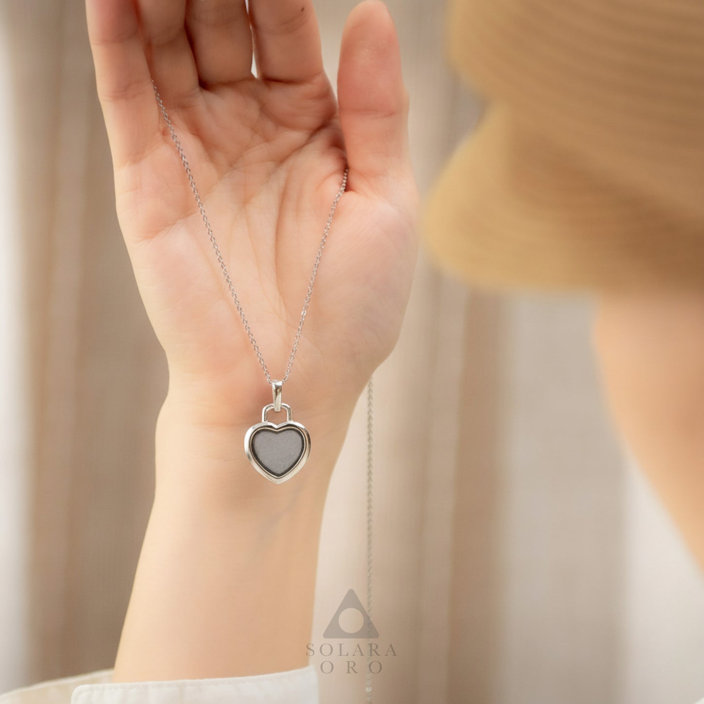 Heart-shaped silver pendant necklace held in a hand with a blurred background