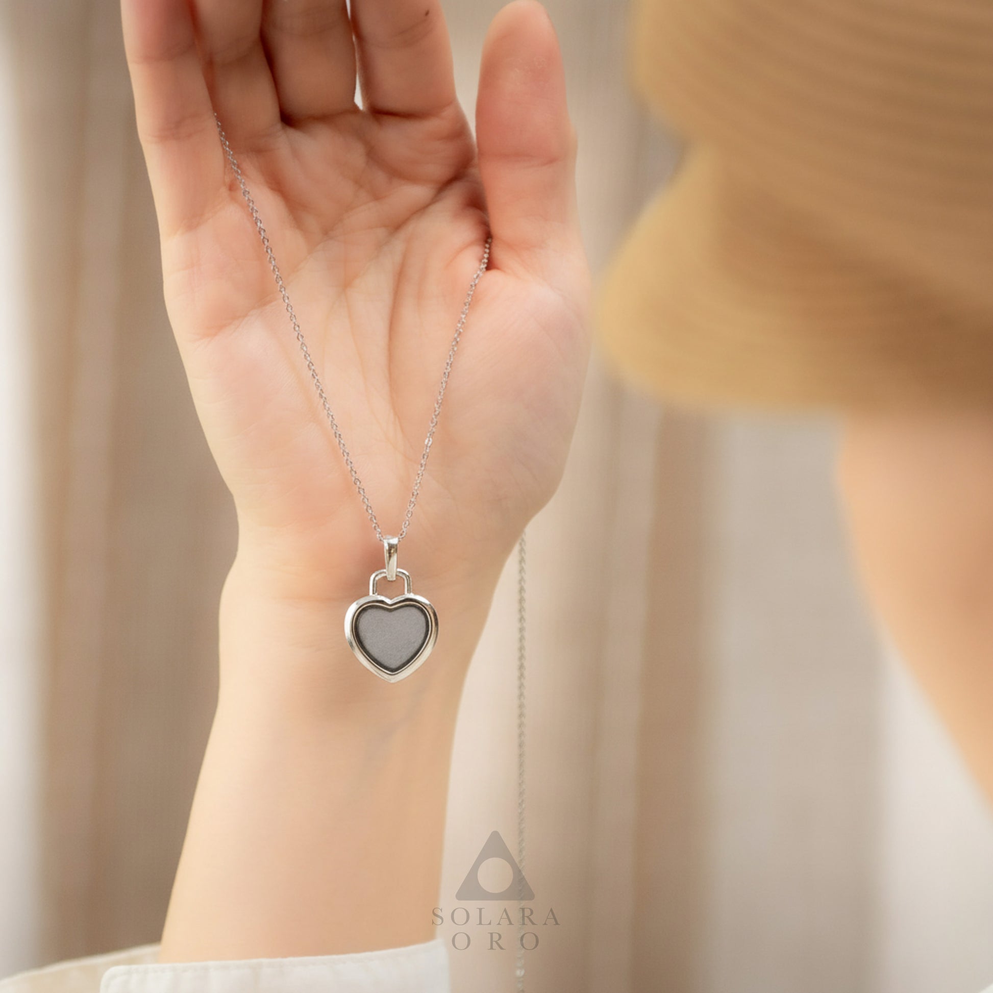 Heart-shaped silver pendant necklace held in a hand with a blurred background
