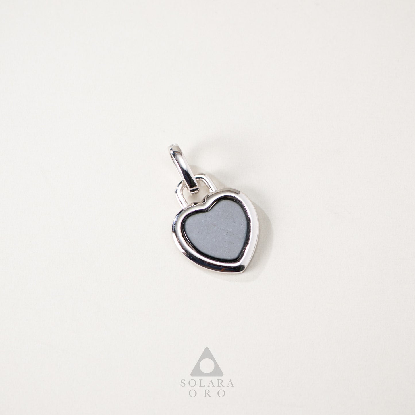 Heart-shaped pendant with gray center on a white background, featuring Solara Oro logo.