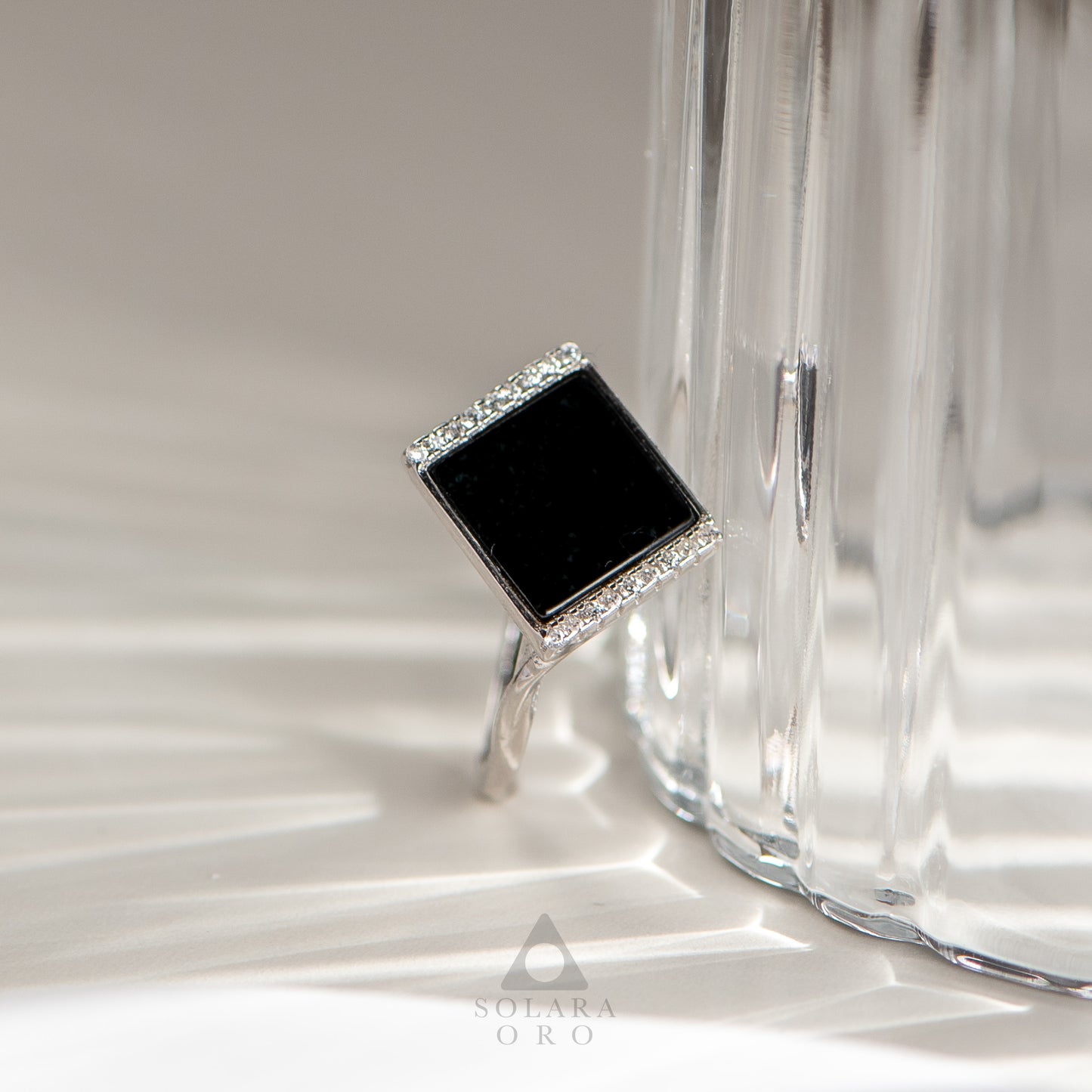 Silver ring with a black square stone and clear stones on a reflective surface