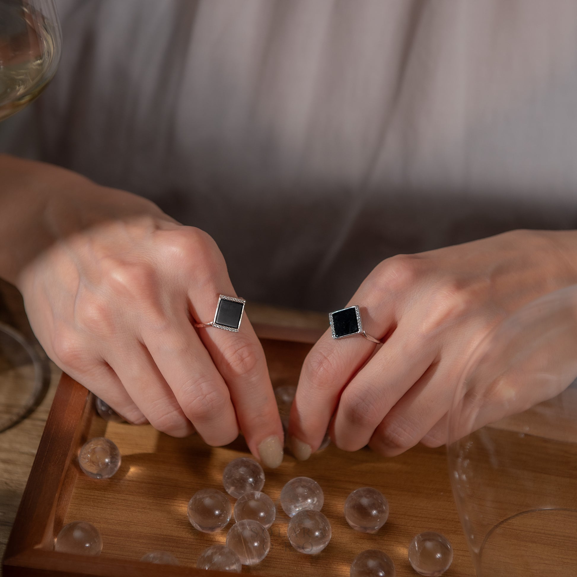 Person wearing square-shaped earrings with clear beads on a wooden surface