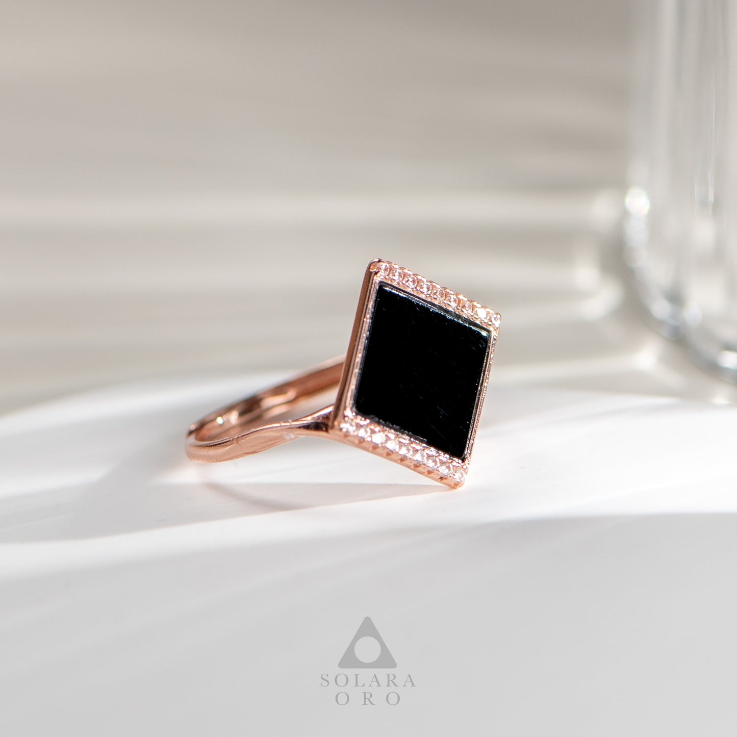 Rose gold ring with a black gemstone on a white surface, branded 'Solara Oro'.