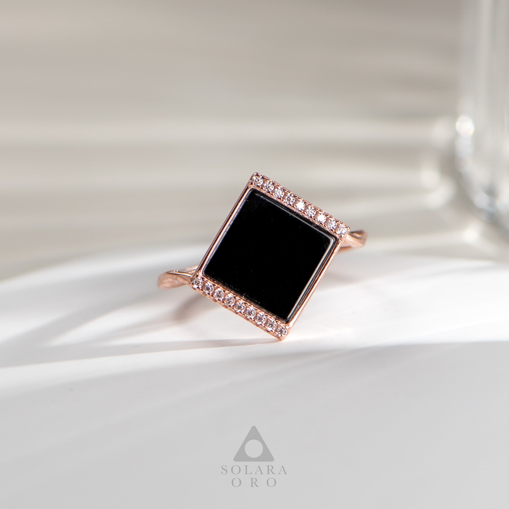 Rose gold ring with a black square stone on a white fabric background