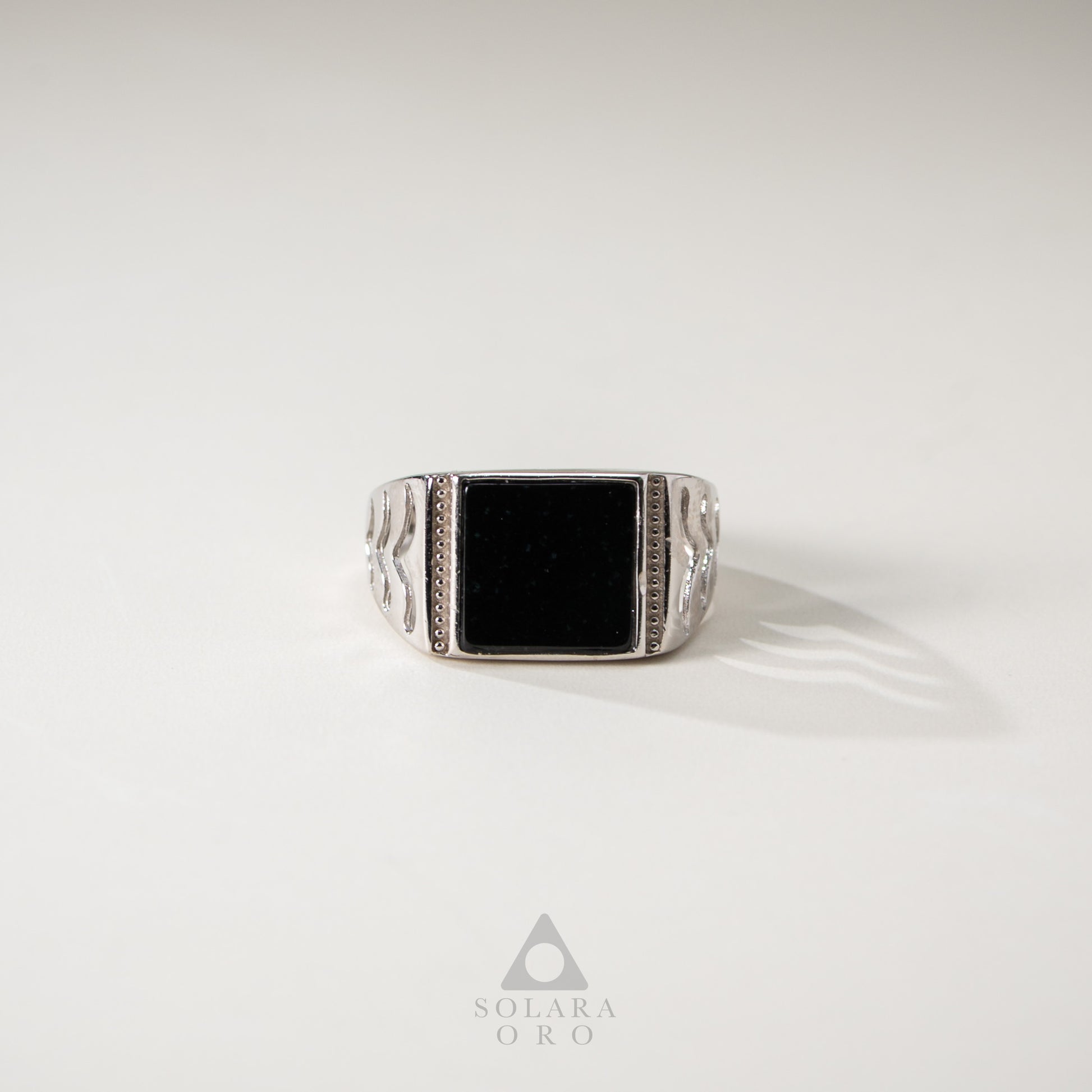 Silver ring with a black stone on a white background, featuring the Solara Oro logo.