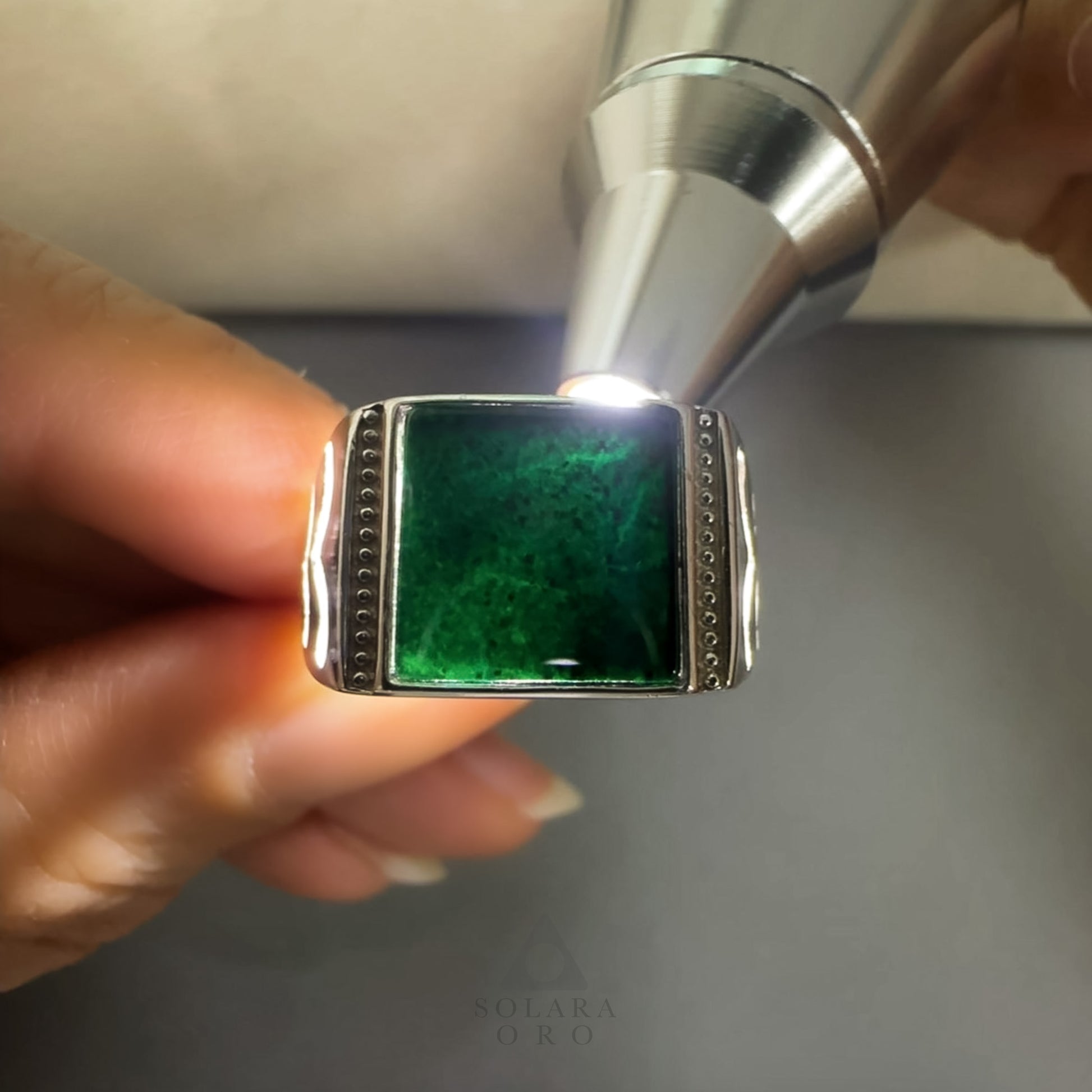 Silver ring with a green gemstone held by a hand against a neutral background