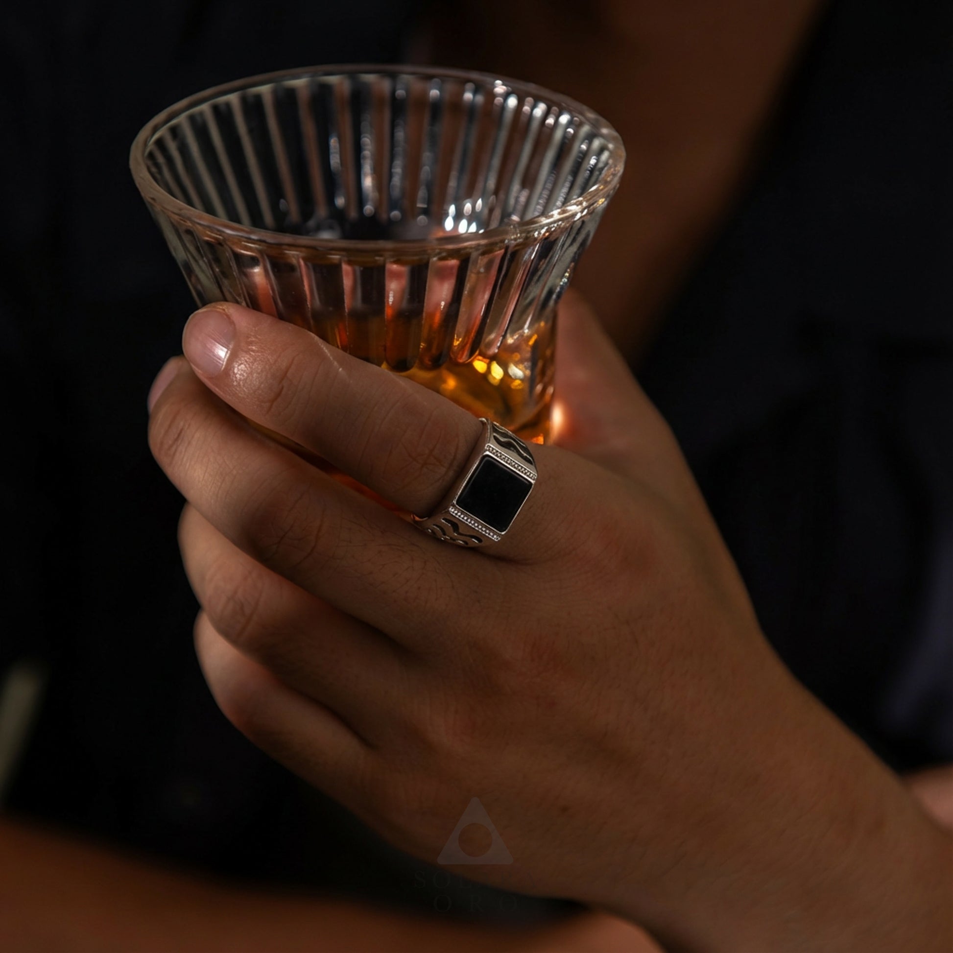 Hand holding a glass of amber liquid with a dark background