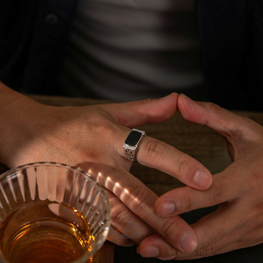 Close-up of hands with a ring holding a glass of amber liquid.