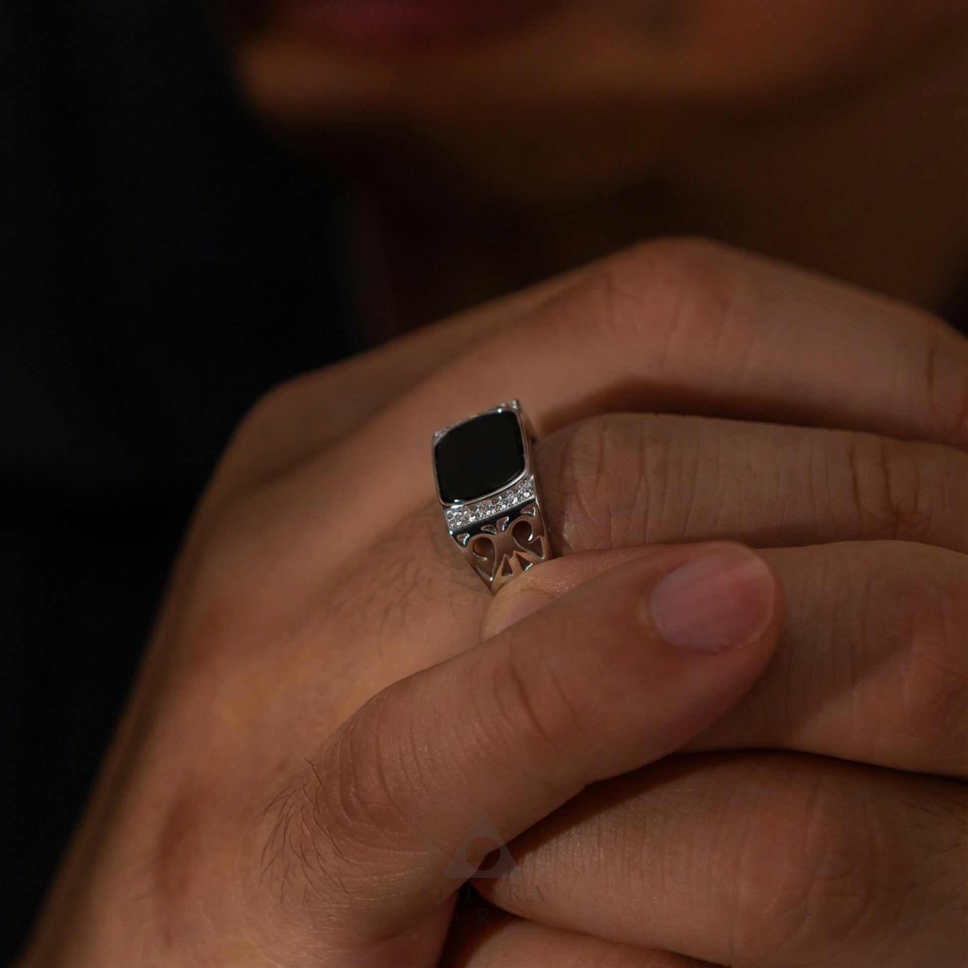 Close-up of a hand wearing a ring with a dark stone on a blurred background