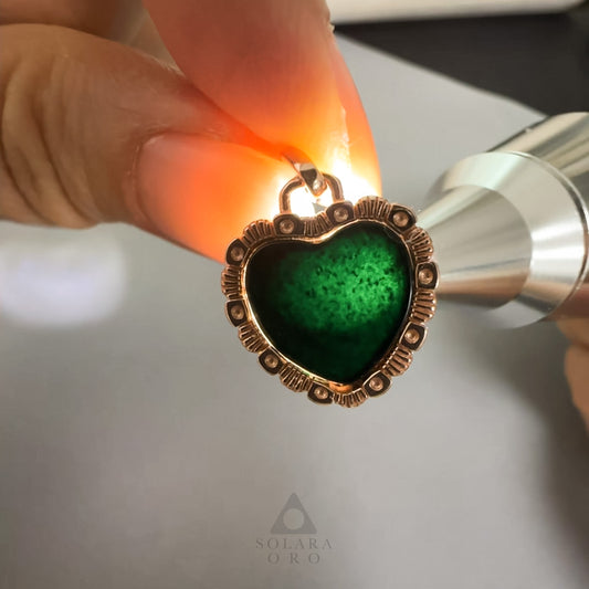 Heart-shaped pendant with green gemstone and gold frame being examined with a magnifying glass.