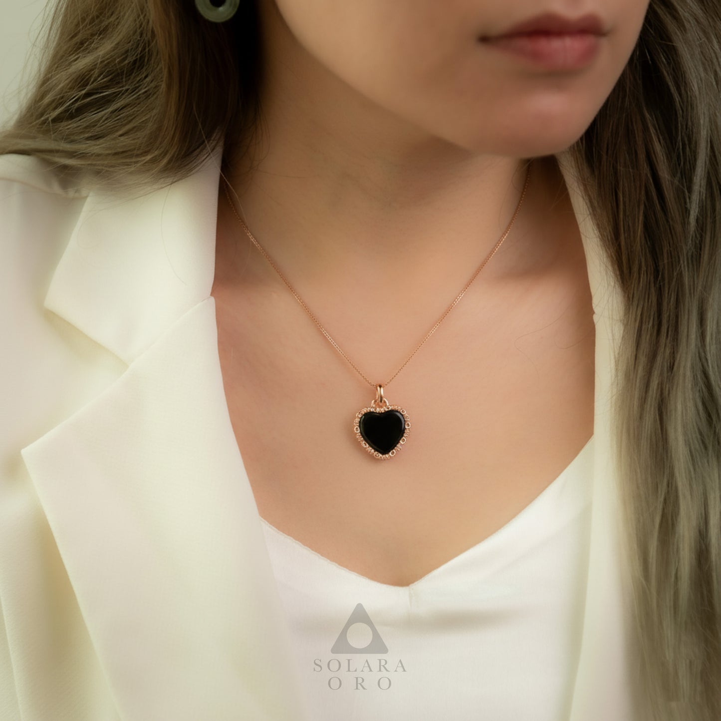 Close-up of a person wearing a necklace with a black heart pendant, branded 'Solaara Oro'.