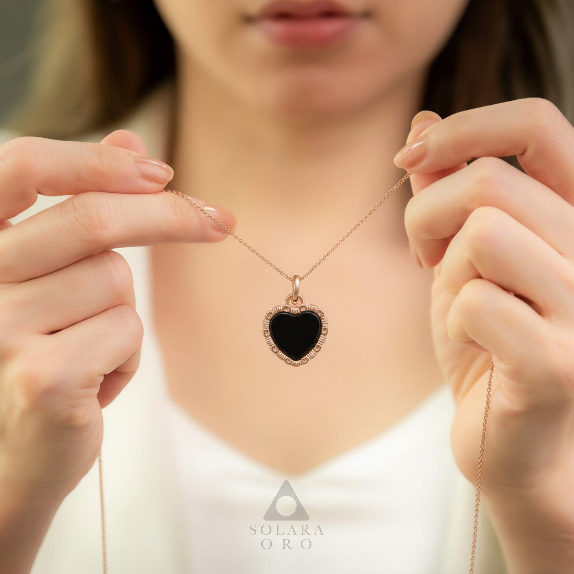 Heart-shaped necklace with a black stone held by hands, brand 'Solerara Oro' visible.