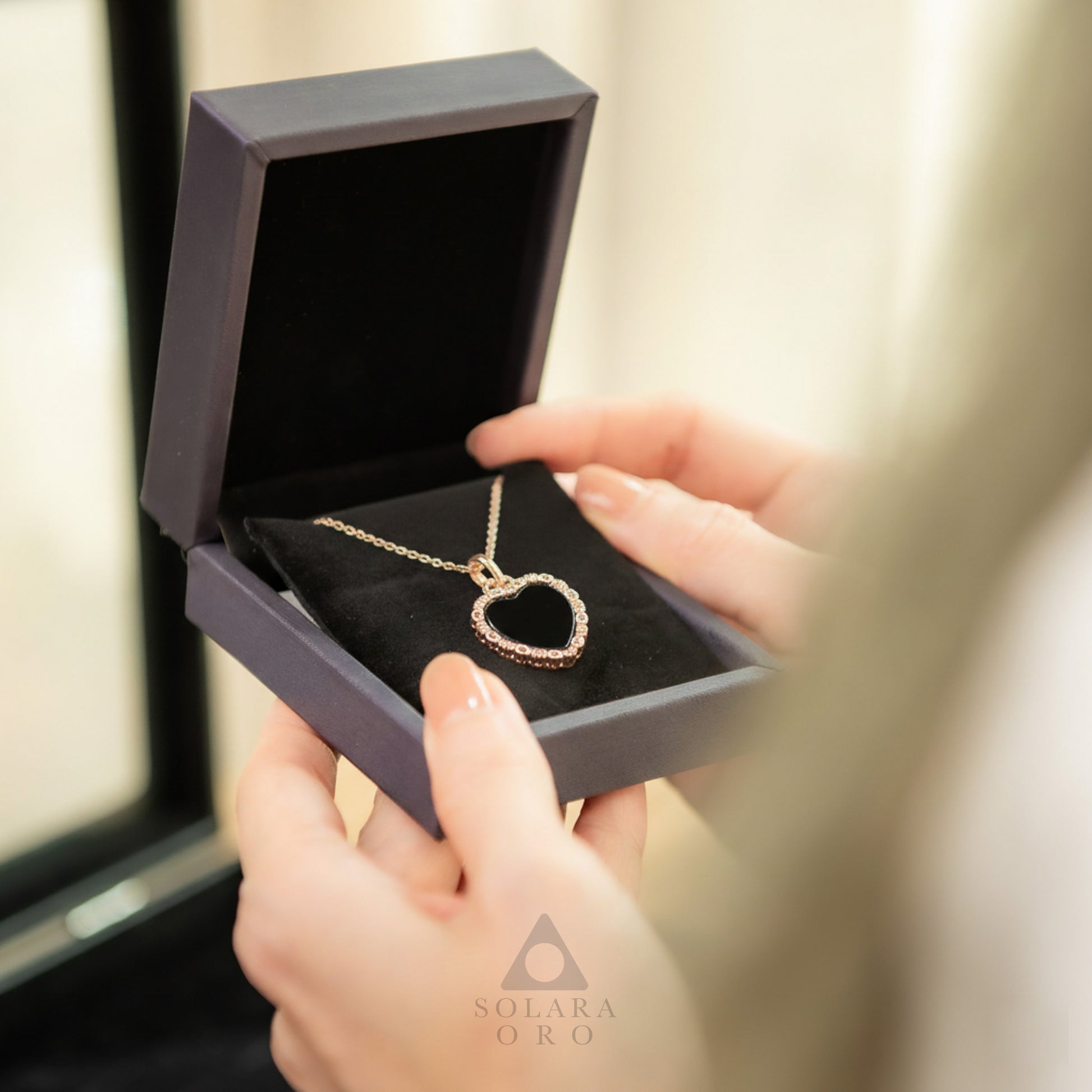 Heart-shaped necklace in a purple box held by a person, with 'Solaara Oro' branding.