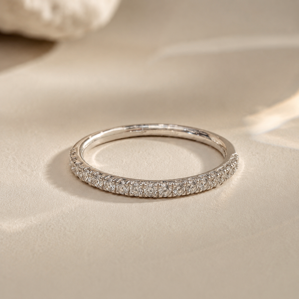Close-up of a thin pavé diamond eternity band in white gold, from The Trilogy ring set, resting on a warm beige surface.