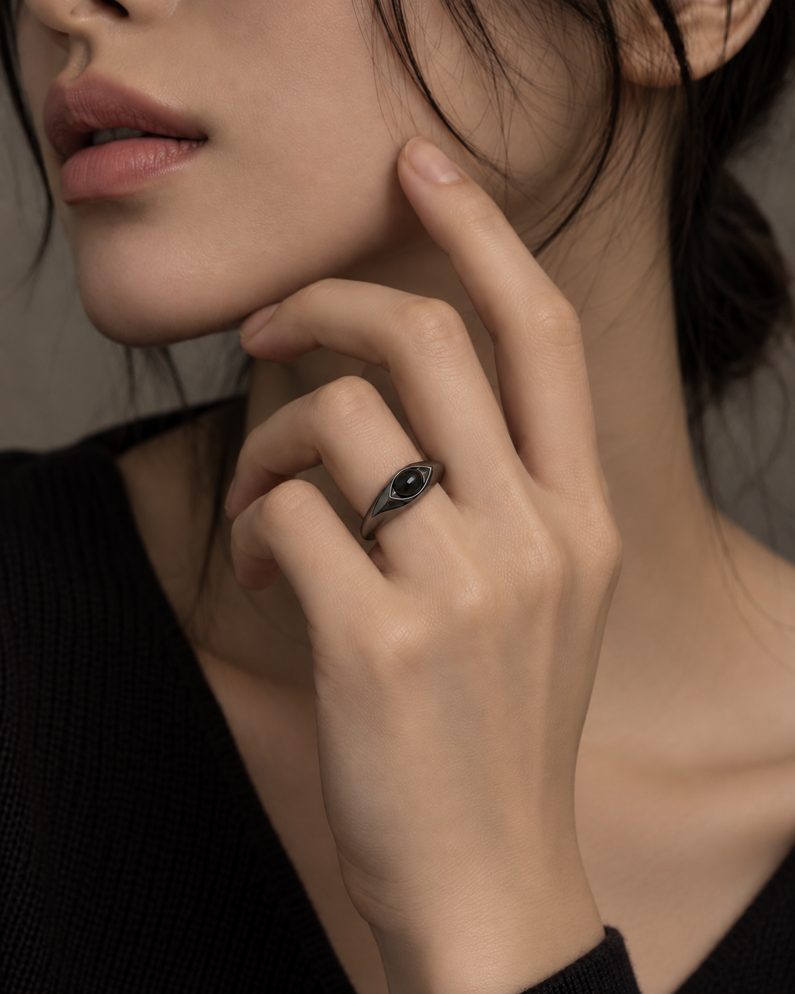 A close-up lifestyle shot of a model wearing a dark metallic ring with a central black oval stone on her finger.