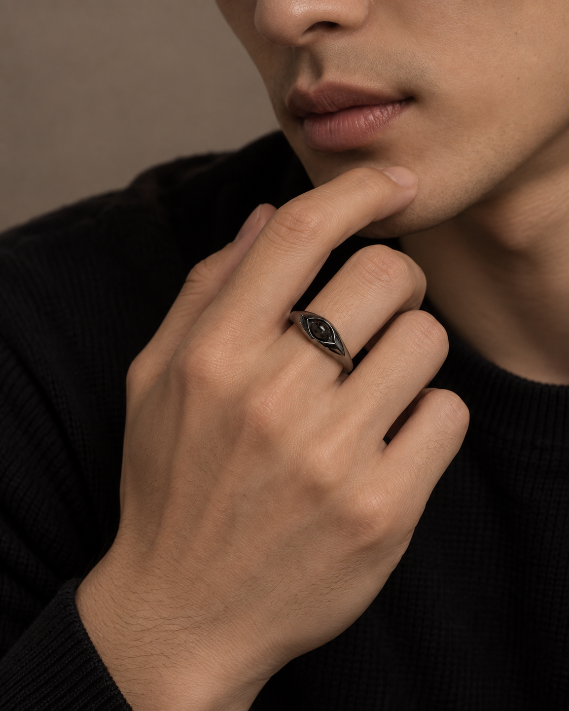 A close-up lifestyle shot of a man wearing a dark metal signet ring with a black inlay on his ring finger, set against a dark sweater and a neutral background.