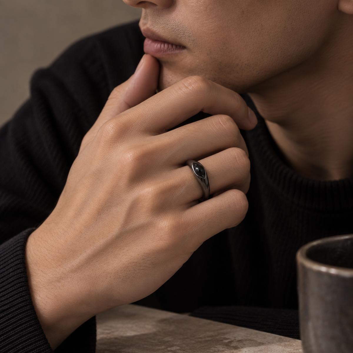 A close-up lifestyle shot of a man wearing a dark metallic ring with a black inlay on his ring finger, resting his hand on his chin.
