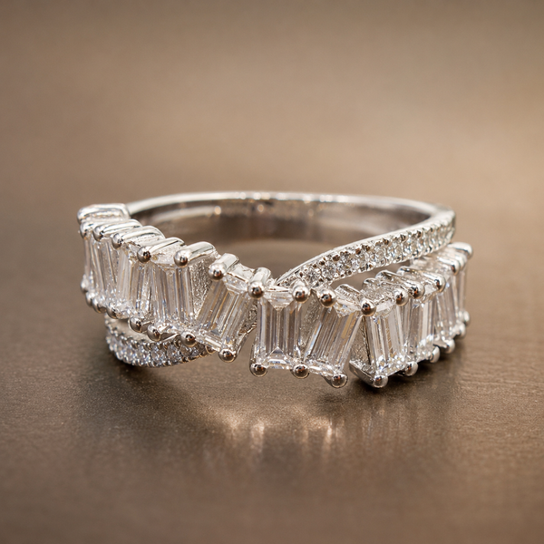 A silver-toned wrap ring featuring baguette-cut clear stones and small accent stones, photographed on a smooth brown surface.