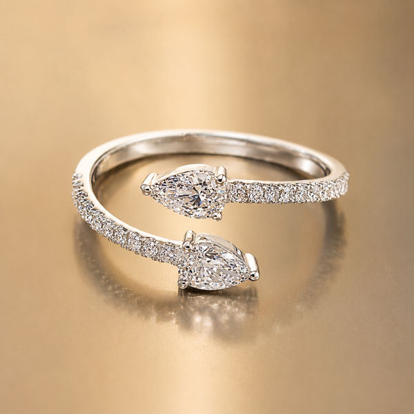 A silver-toned open ring with two marquise-cut diamond centers and pavé-set diamond bands, photographed on a warm gold reflective surface.