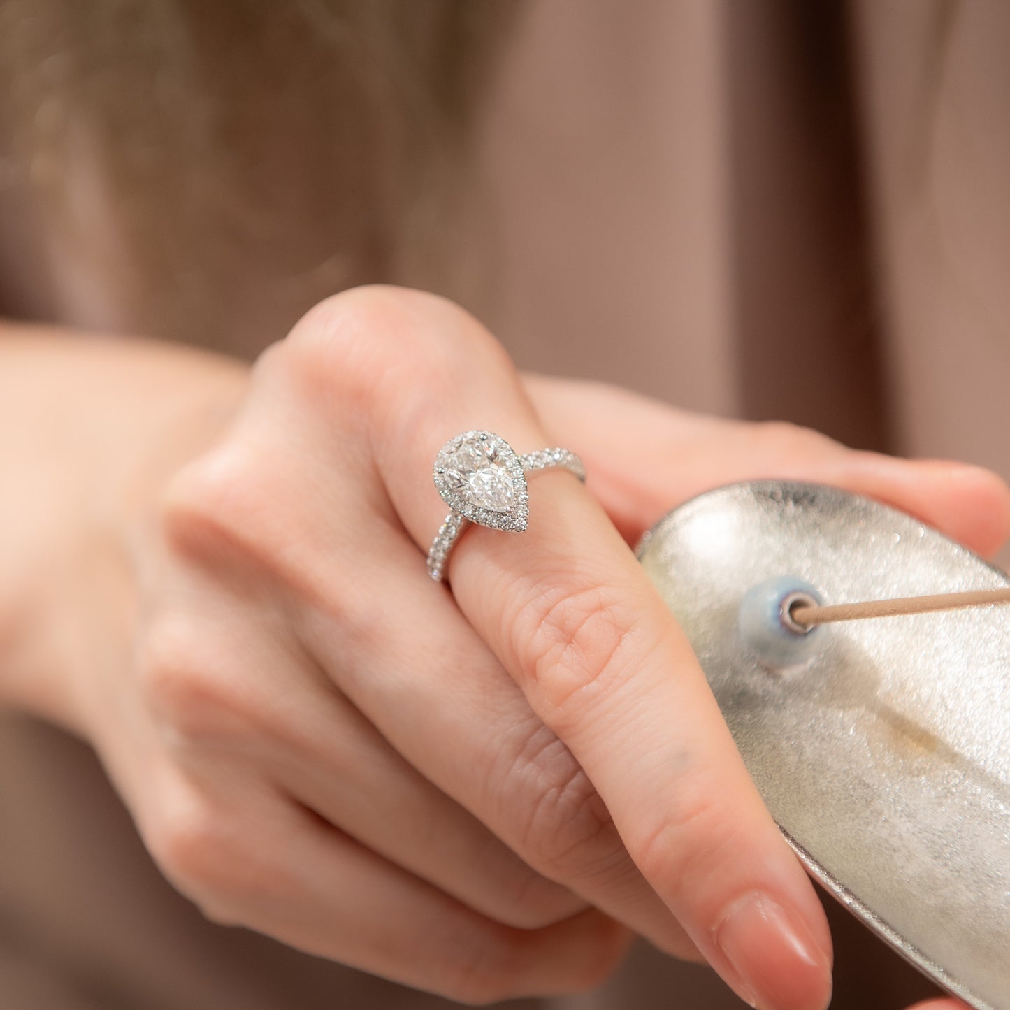 Close-up of a hand wearing a silver ring with a diamond, holding a metallic object.