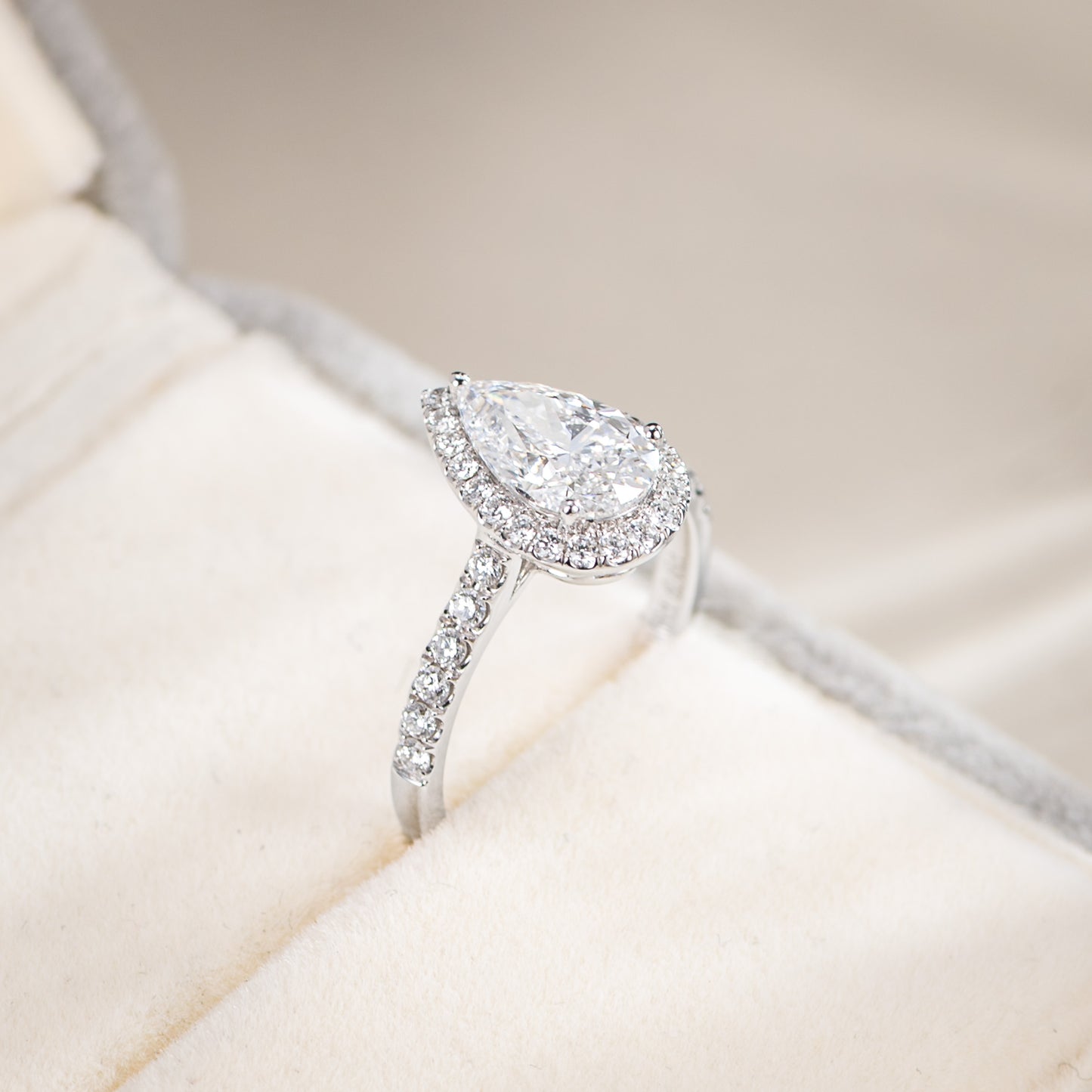 Diamond ring with pear-shaped center stone on a soft beige background