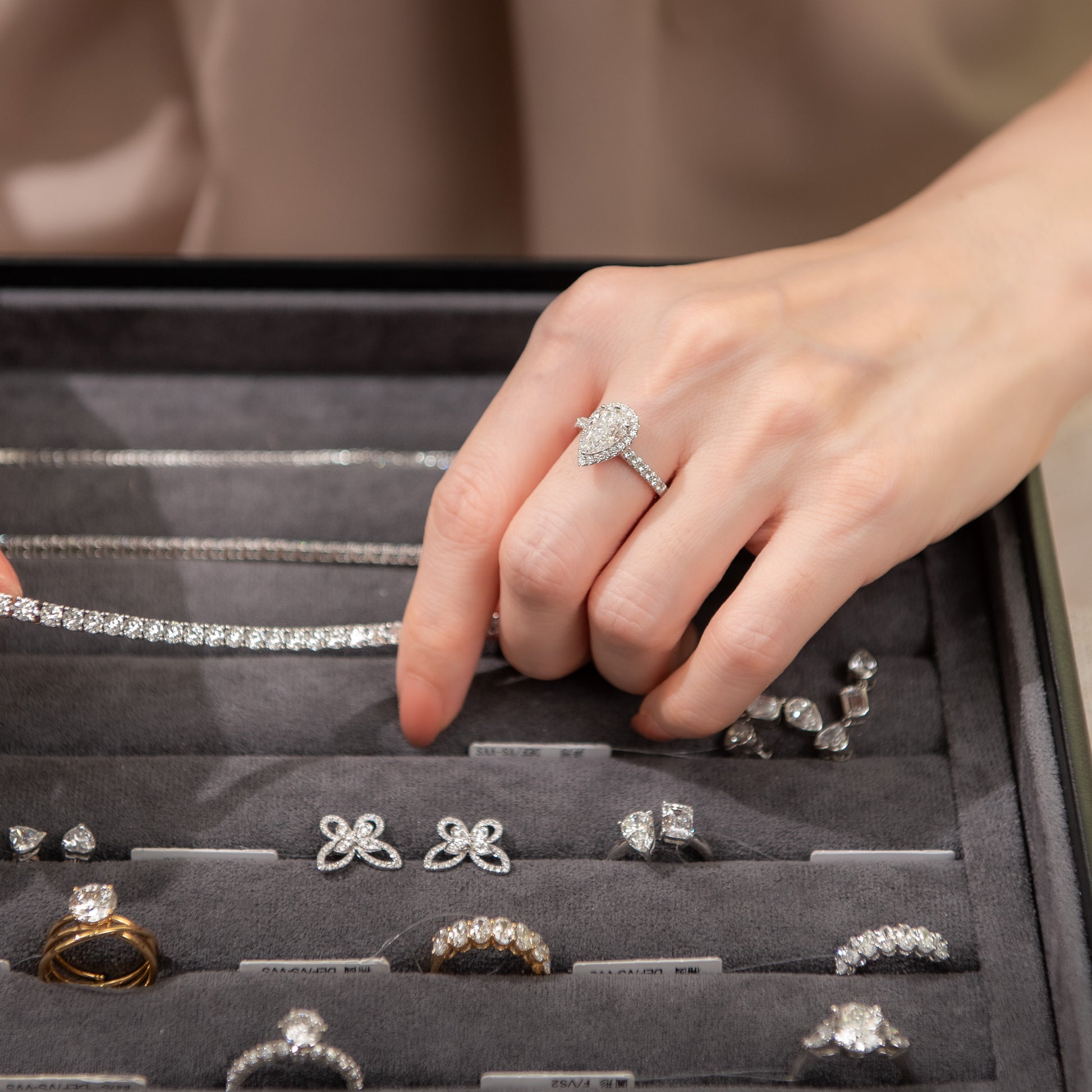 Hand with a diamond ring touching jewelry in an open display case.