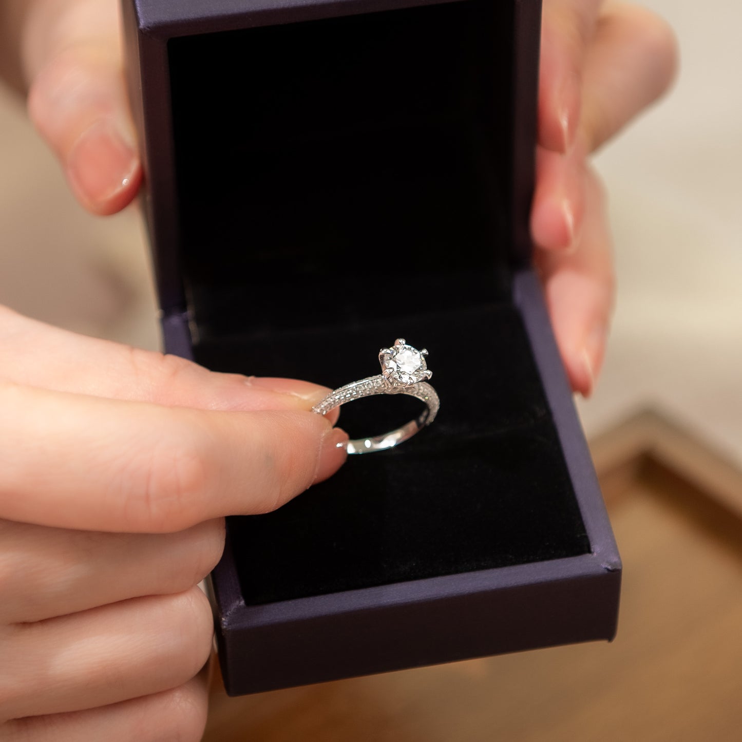 Silver ring with a diamond held by a hand above an open jewelry box.