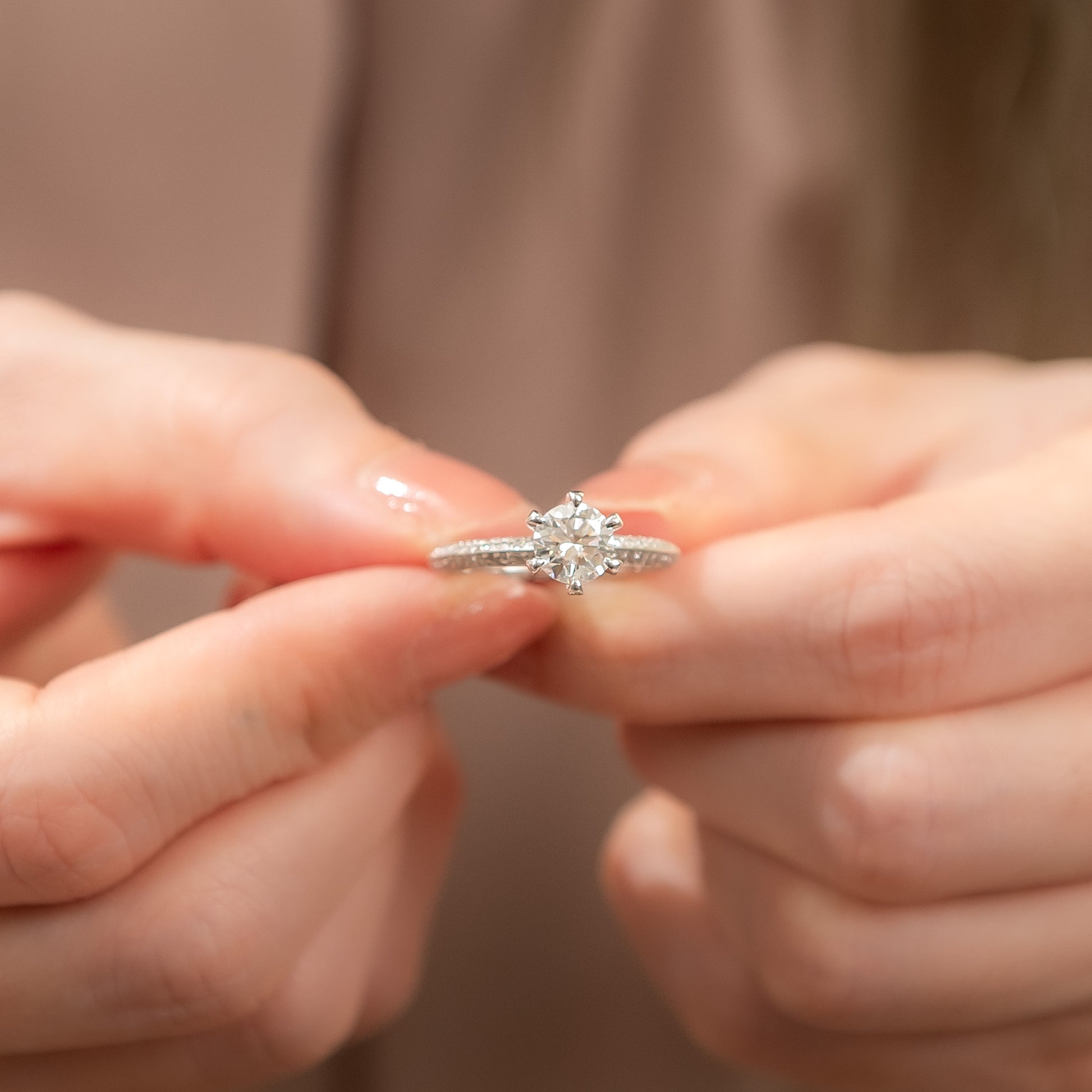Close-up of hands holding a diamond ring against a neutral background
