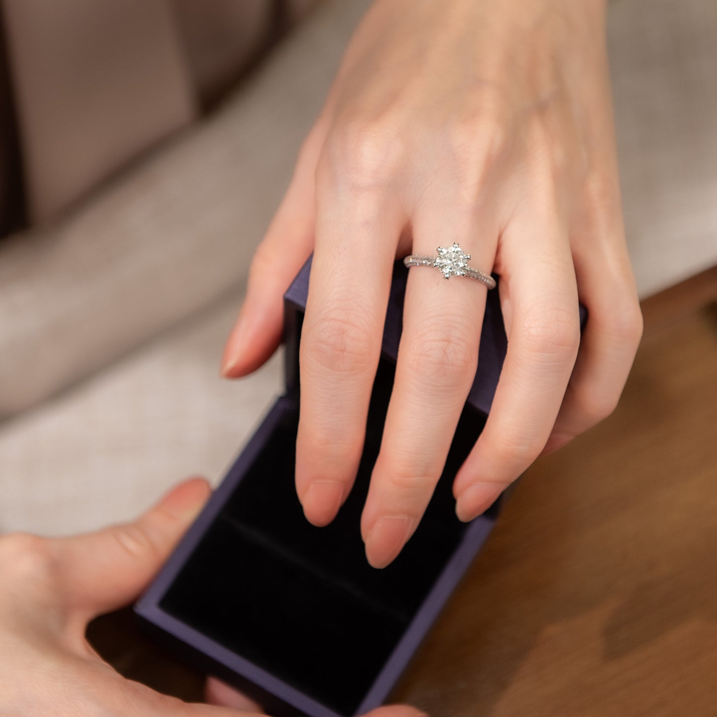 Hand holding a diamond ring with another hand opening a purple box.