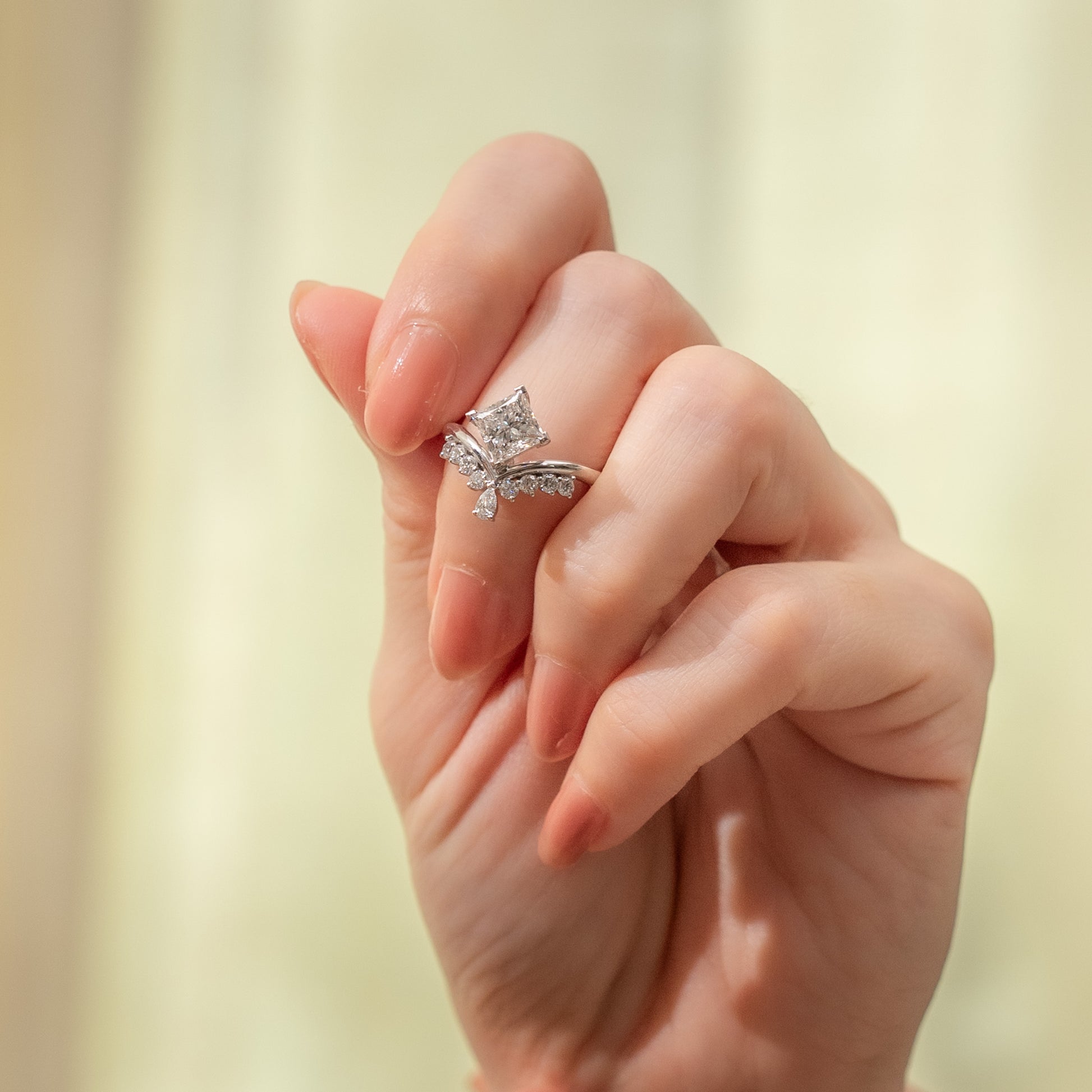 Hand wearing a silver ring with a diamond on a blurred background
