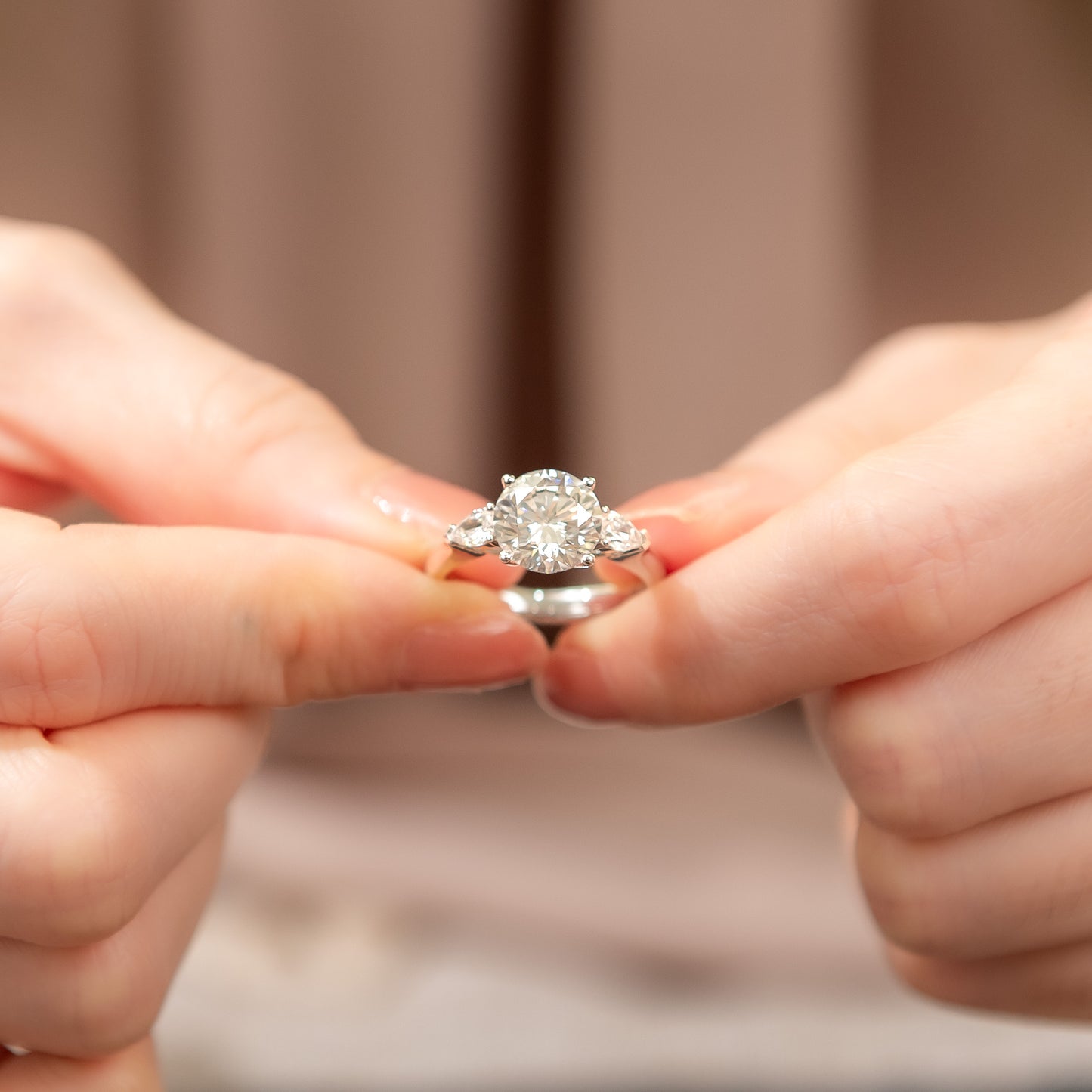 Diamond ring held between two hands against a neutral background