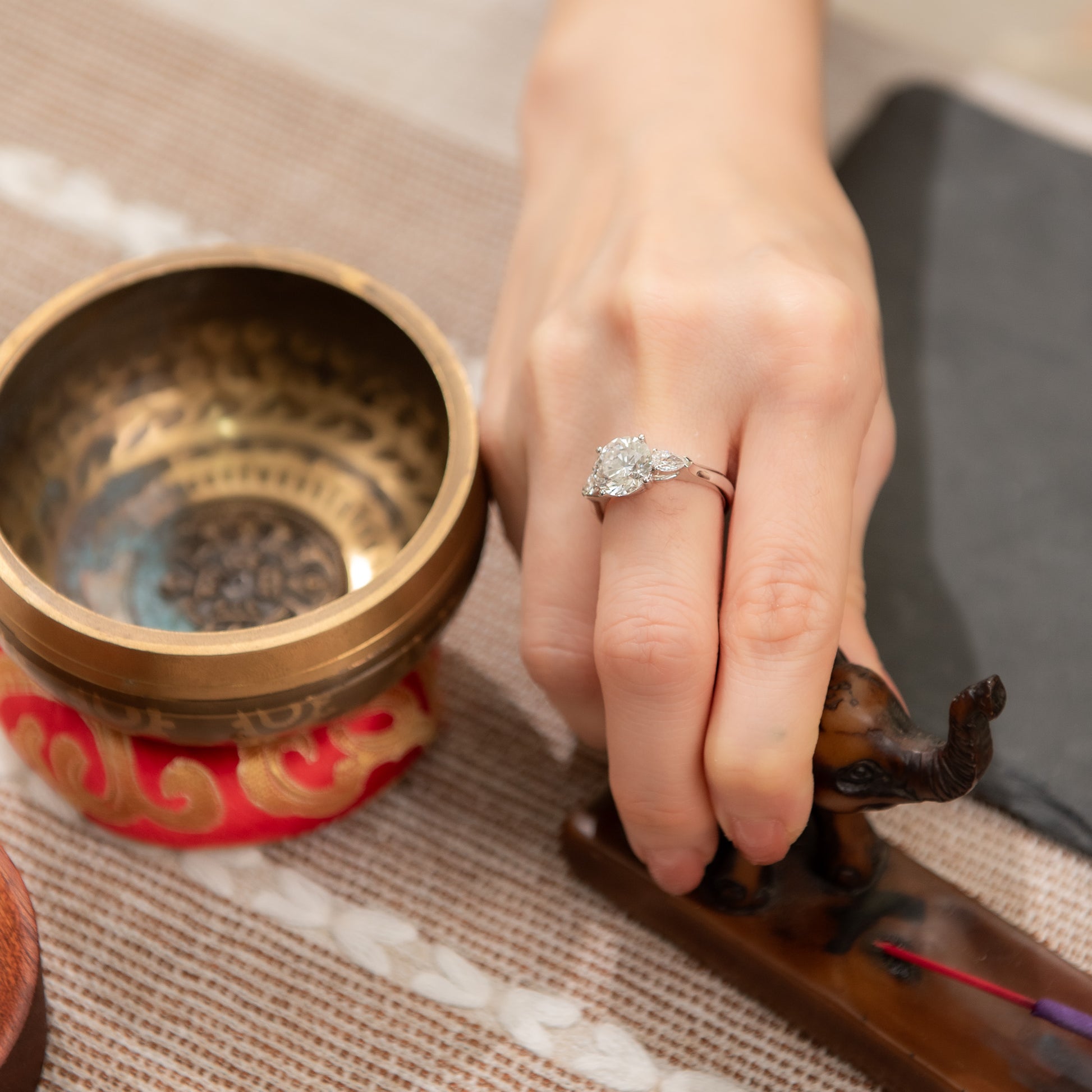 Hand with a ring holding a wooden object next to a decorative bowl on a textured surface