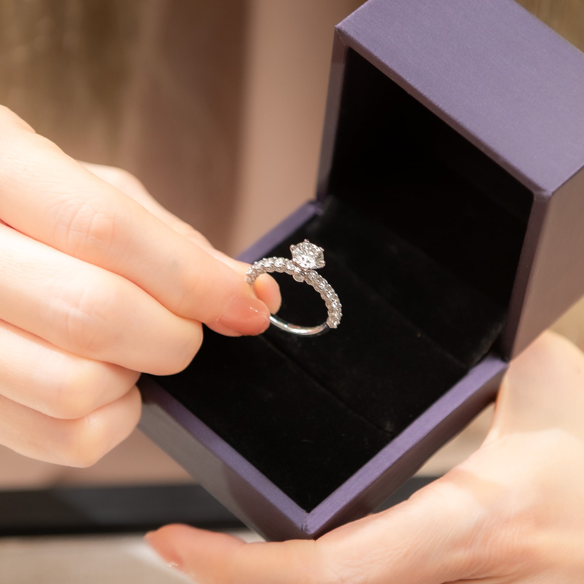 Person holding a diamond ring above an open purple jewelry box.