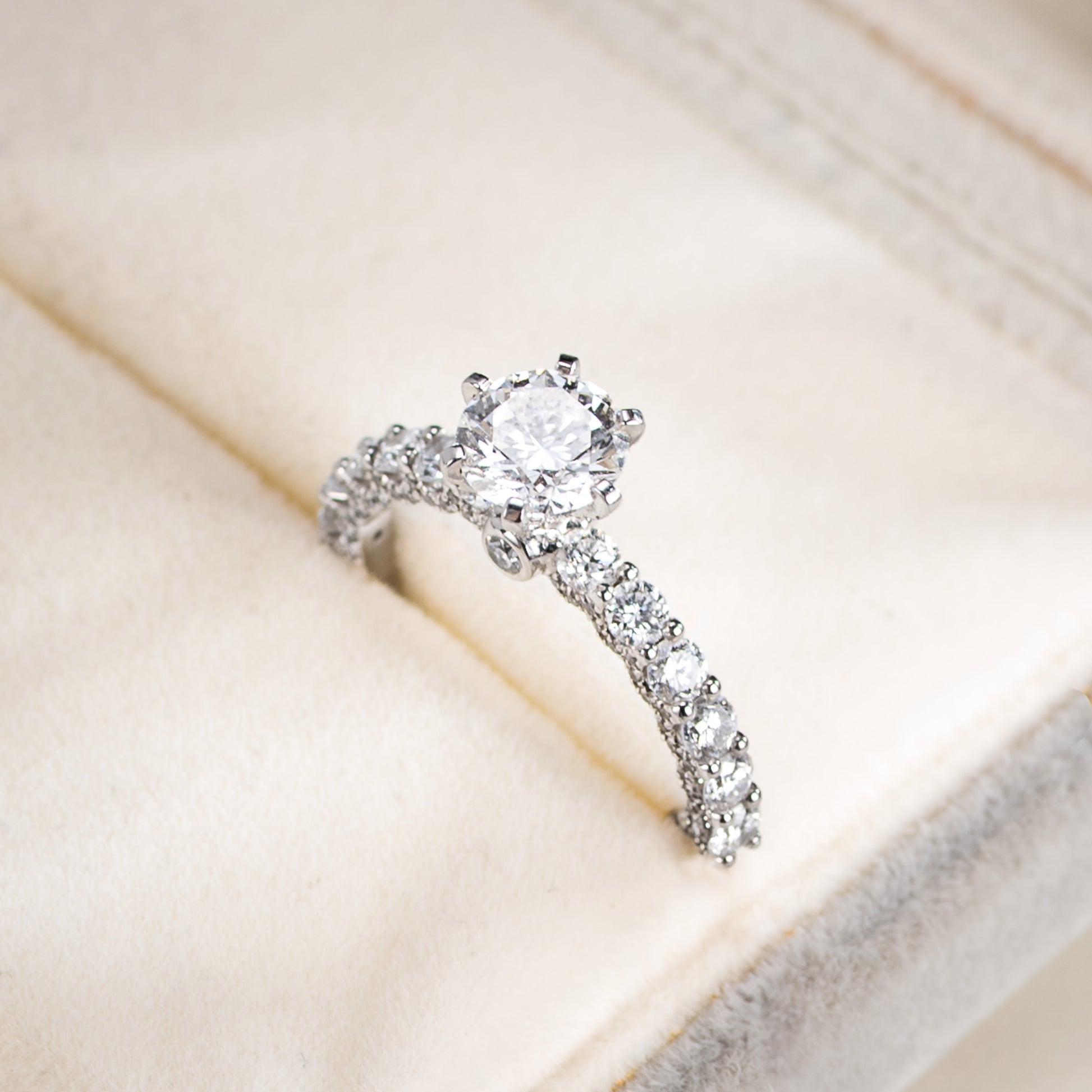 Silver ring with a central diamond and smaller diamonds on a beige surface